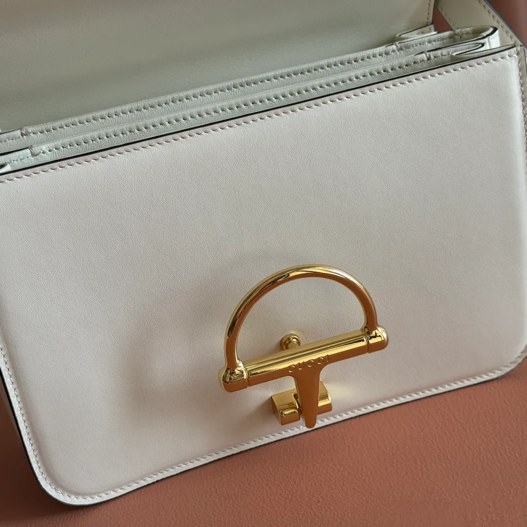 p1640. 💋💋💋【With full set of original counter packaging】2025 autumn and winter series, the Gucci Siena series small shoulder bag continues the evolution of the iconic element of Gucci's classic horsebit. Crafted from fine glossy leather, this shoulder bag has a structured shape and a half-horsebit buckle design from the 1970s. Finished with gold-tone hardware, the interior is lined with three levels of gusseting and a zipped pocket. Black fine glossy leather Gold-tone hardware Black leather lining Interior: 3-level fastening and 1 zipped pocket Shoulder straps: Height: 23cm – 25cm; Length: 127cm Half-horsebit snap fastener Ident: 846705. Dimensions: 22.5cm (width) x 14cm (height) x 8cm (depth) Weight: approx. 0.7kg Color: White full leather. Made in Italy