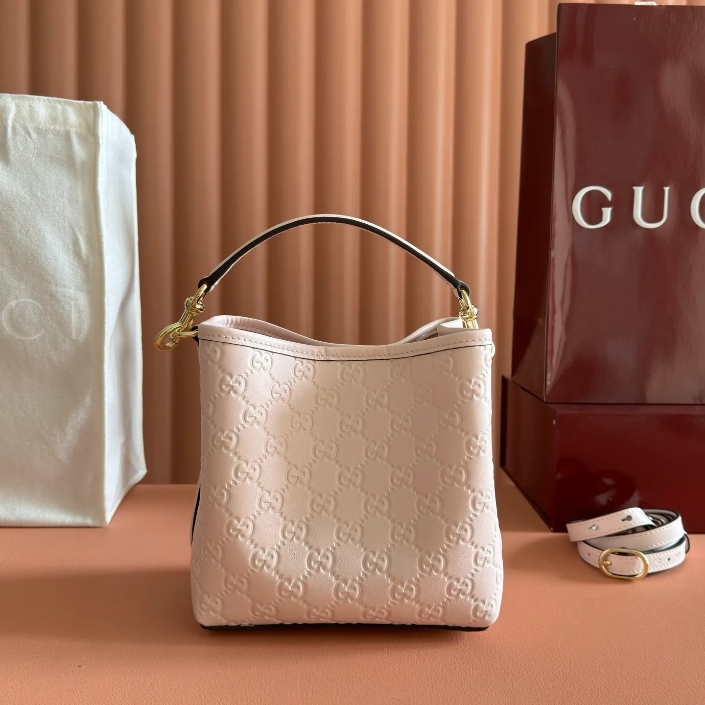 p1140. 💋💋💋【With full set of original counter packaging】GG Emblem series reinterprets the brand's timeless elegance and exquisite craftsmanship. Lined in webbed cotton, this bucket bag features an internal compartment for added functionality. Apricot pink GG printed embossed calf leather Light gold tone hardware Taupe cotton and linen lining Additional D-ring for attaching removable items Interior: two compartments and a central snap compartment Top handle with hook closure (height: 14 cm) Removable and adjustable calf leather shoulder strap (height: 52 cm - 57.5 cm; length: 107 cm - 114 cm) Magnetic snap closure Ident No.: 815118. Dimensions: 19cm (W) x 18cm (H) x 11cm (D) Weight: Approx. 0.45kg Color: Apricot Pink/Embossed. Made in Italy