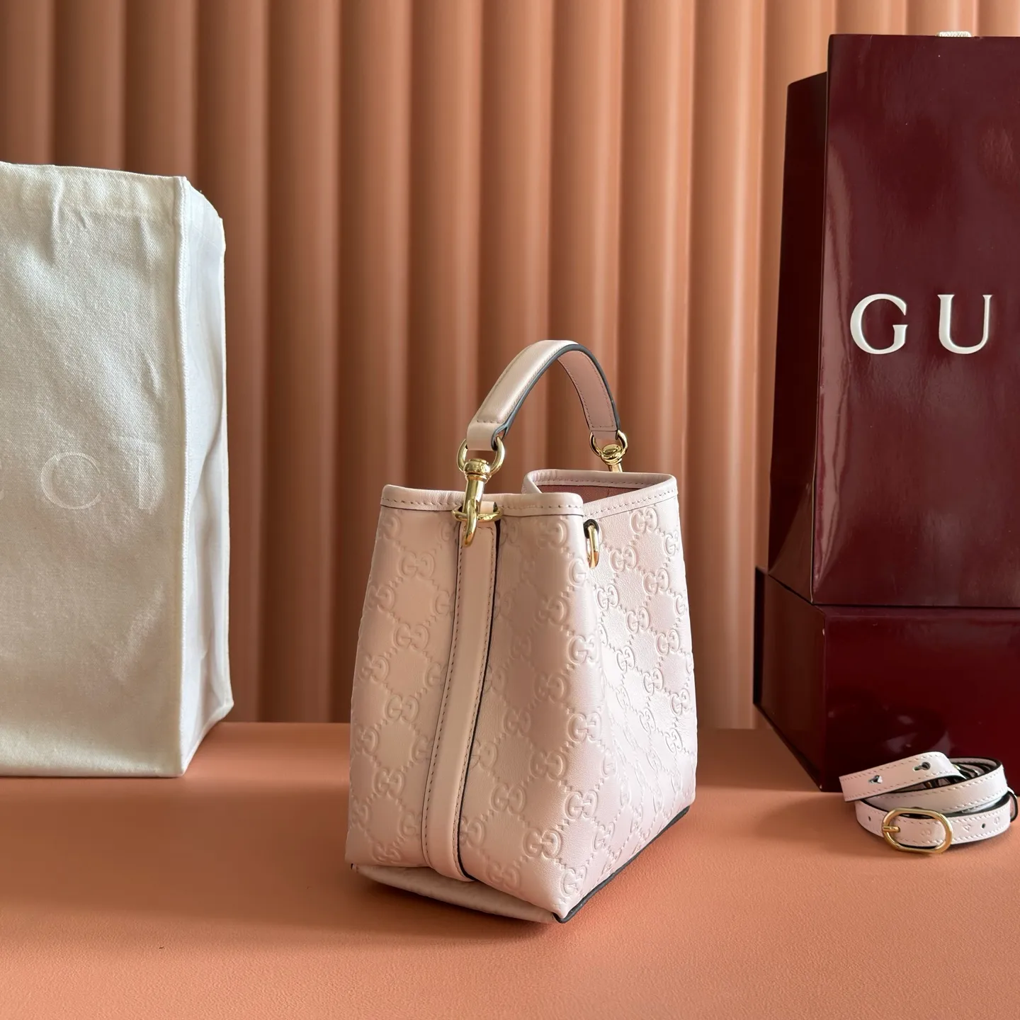 p1140. 💋💋💋【With full set of original counter packaging】GG Emblem series reinterprets the brand's timeless elegance and exquisite craftsmanship. Lined in webbed cotton, this bucket bag features an internal compartment for added functionality. Apricot pink GG printed embossed calf leather Light gold tone hardware Taupe cotton and linen lining Additional D-ring for attaching removable items Interior: two compartments and a central snap compartment Top handle with hook closure (height: 14 cm) Removable and adjustable calf leather shoulder strap (height: 52 cm - 57.5 cm; length: 107 cm - 114 cm) Magnetic snap closure Ident No.: 815118. Dimensions: 19cm (W) x 18cm (H) x 11cm (D) Weight: Approx. 0.45kg Color: Apricot Pink/Embossed. Made in Italy
