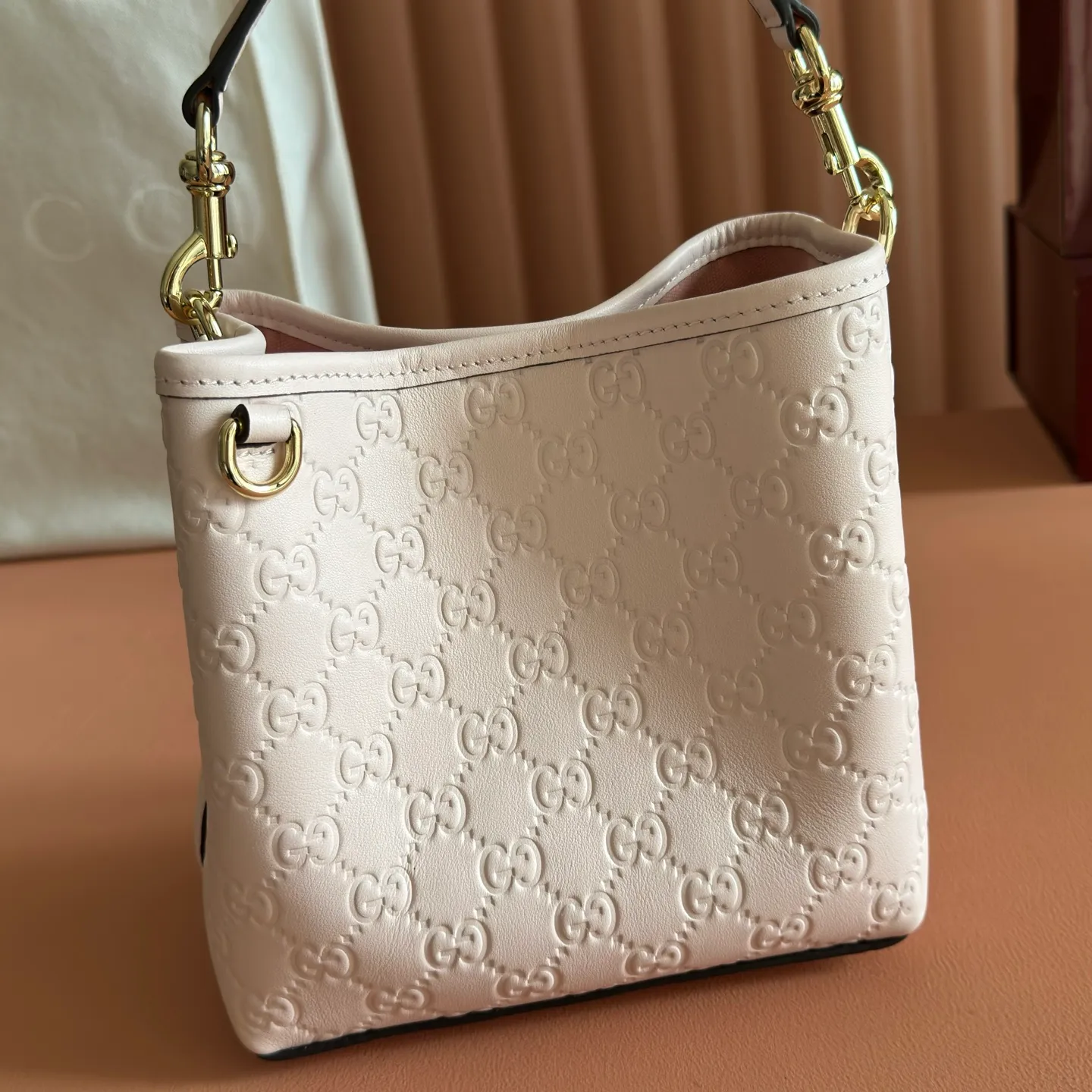 p1140. 💋💋💋【With full set of original counter packaging】GG Emblem series reinterprets the brand's timeless elegance and exquisite craftsmanship. Lined in webbed cotton, this bucket bag features an internal compartment for added functionality. Apricot pink GG printed embossed calf leather Light gold tone hardware Taupe cotton and linen lining Additional D-ring for attaching removable items Interior: two compartments and a central snap compartment Top handle with hook closure (height: 14 cm) Removable and adjustable calf leather shoulder strap (height: 52 cm - 57.5 cm; length: 107 cm - 114 cm) Magnetic snap closure Ident No.: 815118. Dimensions: 19cm (W) x 18cm (H) x 11cm (D) Weight: Approx. 0.45kg Color: Apricot Pink/Embossed. Made in Italy