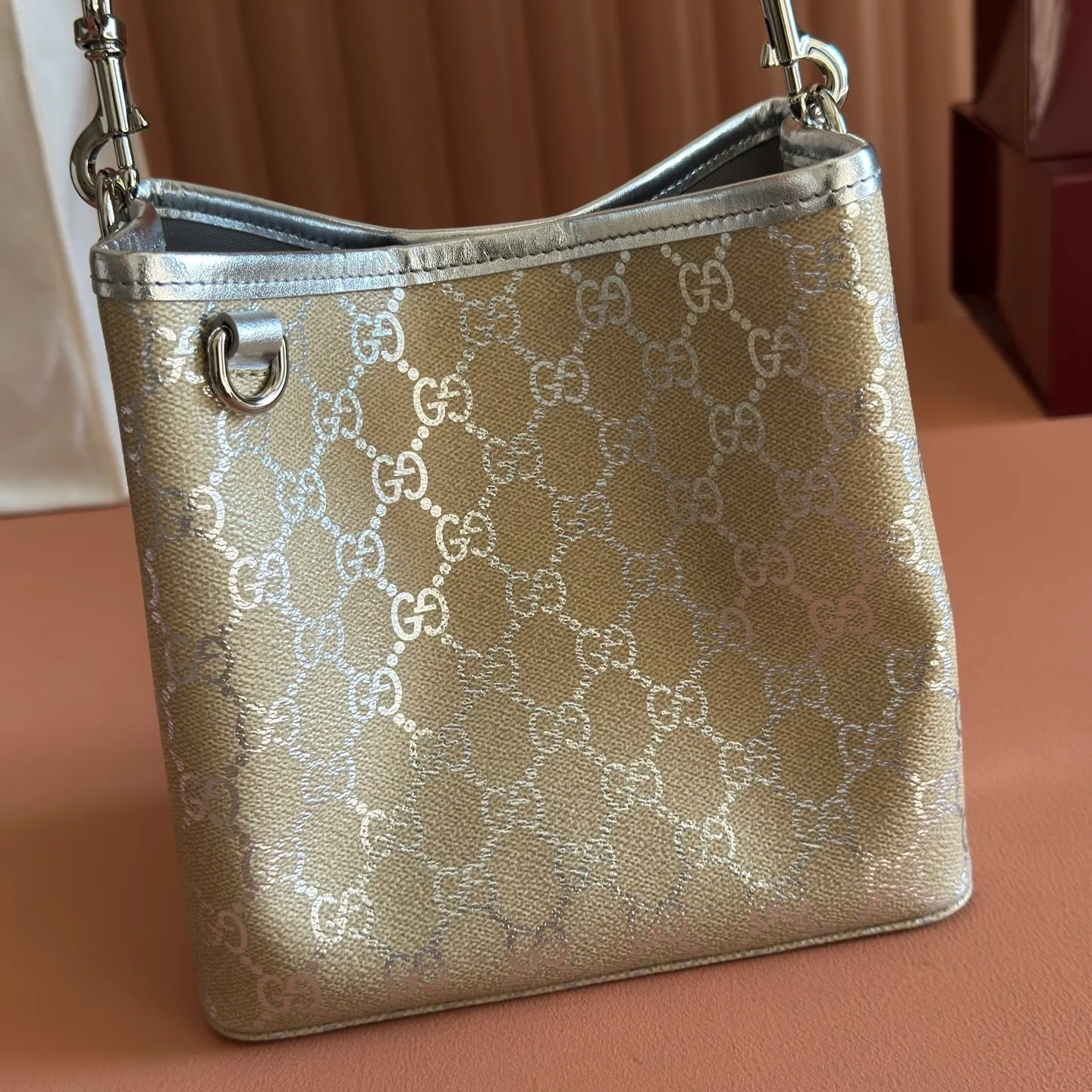 p940💋💋💋【Equipped with full set of original packaging at the counter】The GG Emblem series reinterprets the brand's enduring elegance and exquisite craftsmanship. It uses metallic styles to create a new interpretation of the iconic GG pattern, and is paired with metallic leather piping to complete the overall design. Light beige and silver metallic laminated-effect GG monogram coated fabric Silver metallic leather trim Silver-toned hardware Light gray cotton and linen lining Additional D-ring for attaching detachable items Interior: Two compartments and a central snap-stud compartment Top handle with hook closure (Height: 14cm) Removable and adjustable leather shoulder strap (Height: 52cm - 57.5cm; Length: 107cm - 114cm) Magnetic snap closure Model: 815118. Dimensions: 19cm (W) x 18cm (H) x 11cm (D) Weight: approx. 0.45kg Colour: Light Beige/Silver. Made in Italy