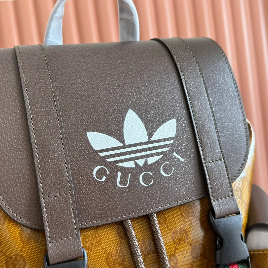 p1300. 📣📣📣【Original leather cabinet complete package】🔥🔥 adidas x Gucci joint series backpack, as one of the adidas x Gucci joint series, this backpack is decorated with Gucci Trefoil print. Adidas and Gucci boldly explore a joint series. The webbing and GG monogram are cleverly combined with the white three stripes and clover logo. The collection is inspired by the creative director’s fond memories of the 1980s and 1990s, integrating the two brands’ rich heritage and iconic design languages ​​to shape the style. Beige and brown GG crystal canvas with Gucci Trefoil print, brown leather adidas x Gucci collection. Red and green webbing, cotton and linen lining. Model: 495563. Dimensions: 34(W) x 42(H) x 16cm(D) Color: Brown/Crystal Canvas co-branded. Made in Italy
