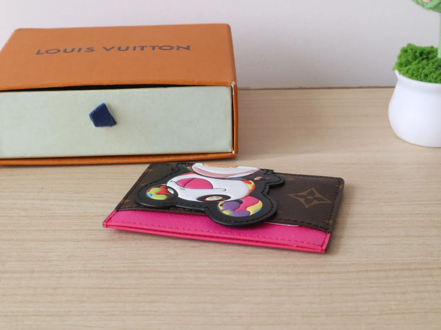 M13439 Card Holder🌟P280 LV x TM Business Card Holder This essential business card holder is reinterpreted with lively details from the Louis Vuitton x Murakami collaboration series, full of joy. The brand's classic Monogram pattern is covered with a bright panda pattern created by Japanese artists, which complements each other with a bright touch of pink on the top. Crafted from coated canvas, the business card holder has a stylish cut and multiple compartments to keep everyday essentials such as business cards and receipts organized.  11 x 7 x 0.5 cm