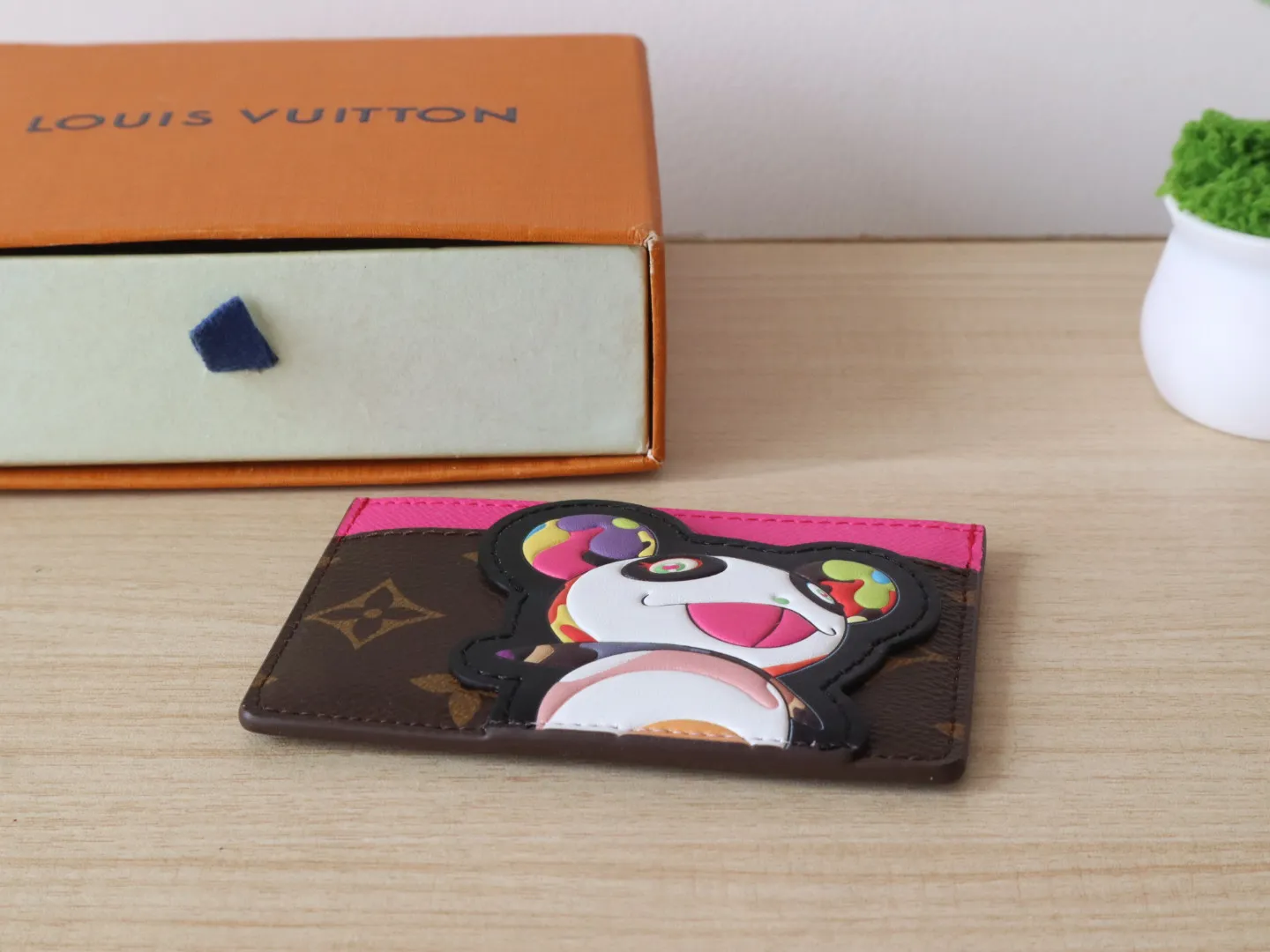 M13439 Card Holder🌟P280 LV x TM Business Card Holder This essential business card holder is reinterpreted with lively details from the Louis Vuitton x Murakami collaboration series, full of joy. The brand's classic Monogram pattern is covered with a bright panda pattern created by Japanese artists, which complements each other with a bright touch of pink on the top. Crafted from coated canvas, the business card holder has a stylish cut and multiple compartments to keep everyday essentials such as business cards and receipts organized.  11 x 7 x 0.5 cm