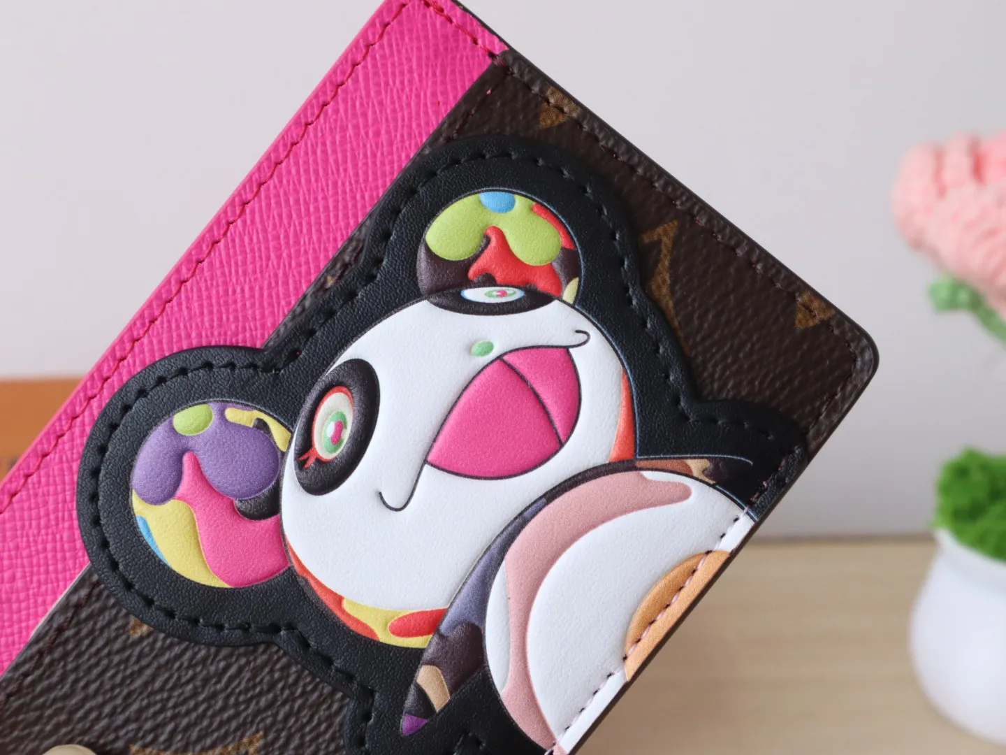 M13439 Card Holder🌟P280 LV x TM Business Card Holder This essential business card holder is reinterpreted with lively details from the Louis Vuitton x Murakami collaboration series, full of joy. The brand's classic Monogram pattern is covered with a bright panda pattern created by Japanese artists, which complements each other with a bright touch of pink on the top. Crafted from coated canvas, the business card holder has a stylish cut and multiple compartments to keep everyday essentials such as business cards and receipts organized.  11 x 7 x 0.5 cm