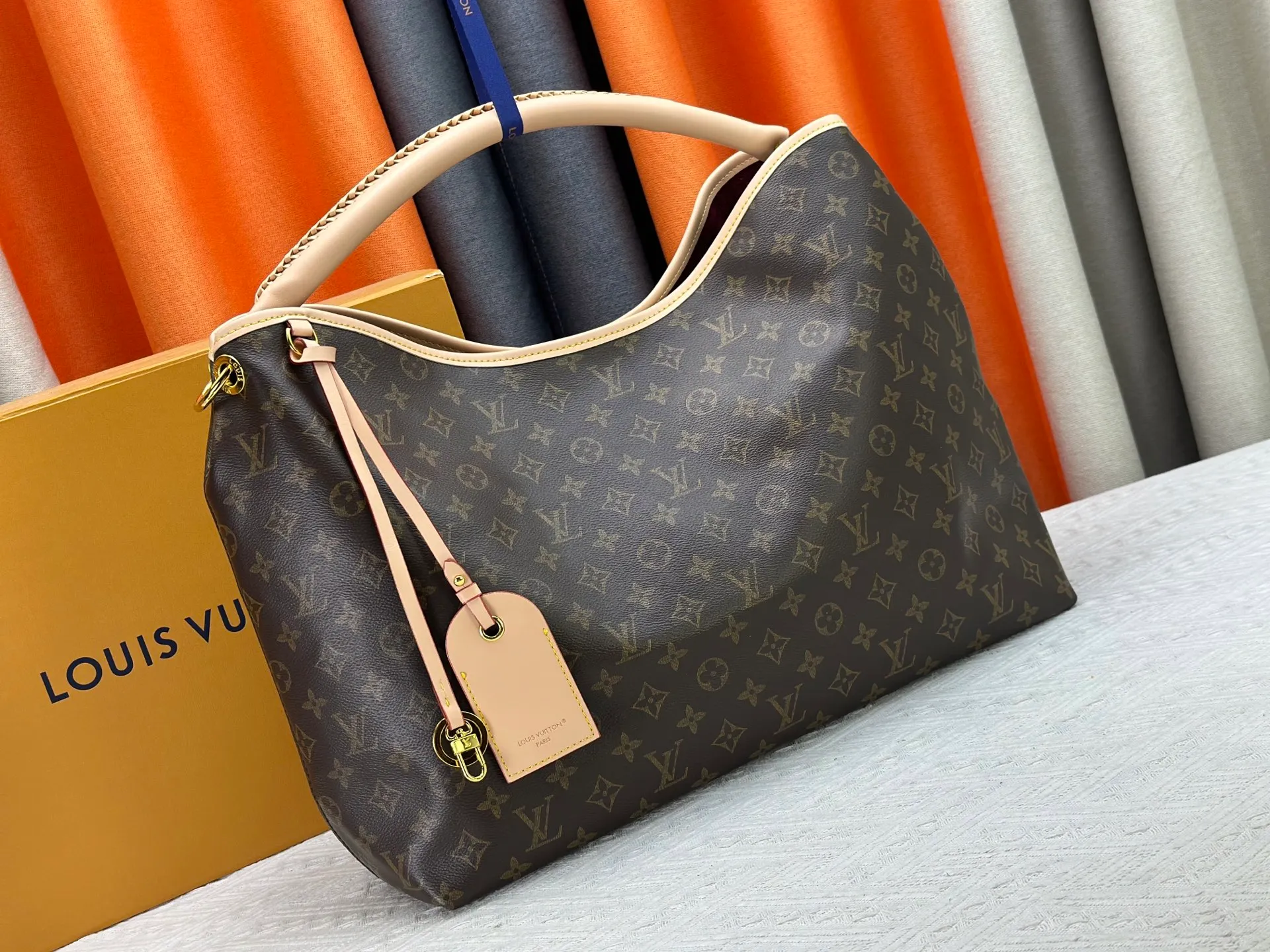 P300 upgrades the original M25877 Again bag, a new interpretation of the iconic Artsy design first launched in 2010, now more flexible, more iconic and more refined. Rooted in LV’s DNA, this bag pays homage to Louis Vuitton’s craftsmanship with its classic Monogram canvas base, hand-woven handles and customizable name tag. It's spacious enough to hold a laptop and opens to reveal multiple pockets. Gold hooks can be used to hang playful accessories! ! Size:50x30x15.5CM