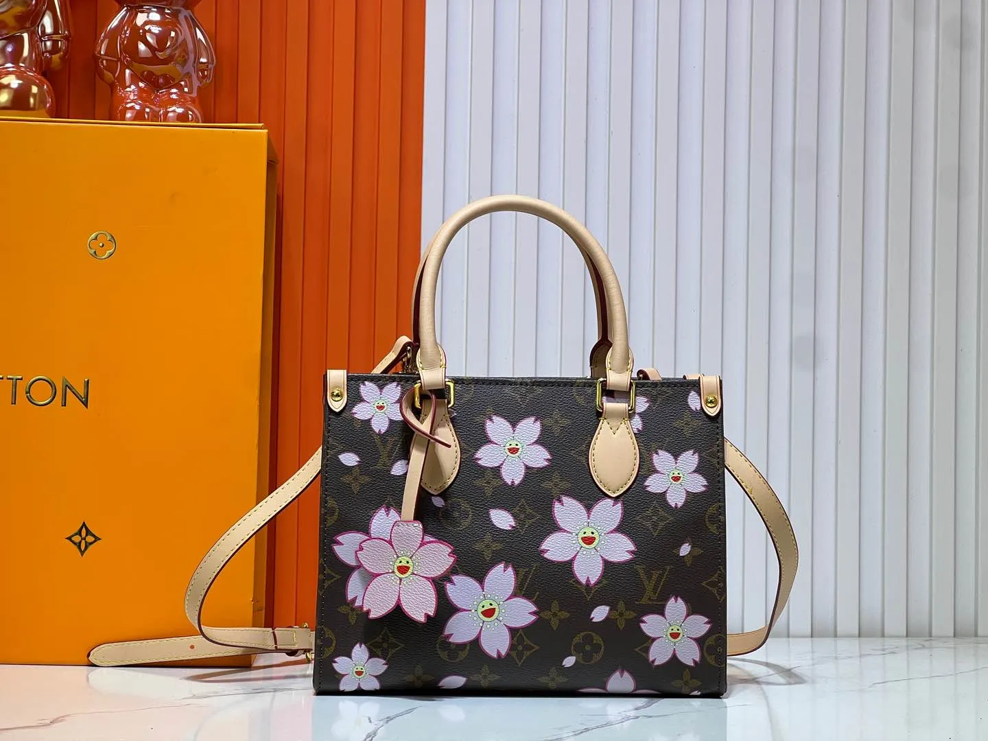 Batch 260💰M45659 M13668!🔥Lv&Takashi Murakami🐼Sakura🌸OnTheGo small new version The legendary ONTHEGO handbag: always able to meet your various needs for handbags. It has a large capacity but is not bulky. It is stiff and soft to the touch, making it suitable for home and travel. Tighten the side ties and it instantly transforms into a stylish urban handbag. Loosen the straps and it transforms into a chic and practical handbag. The slender leather handle can be carried over the shoulder or between the arms. The model shown here is made of Damier Azur canvas. Size: 25x11x19cm