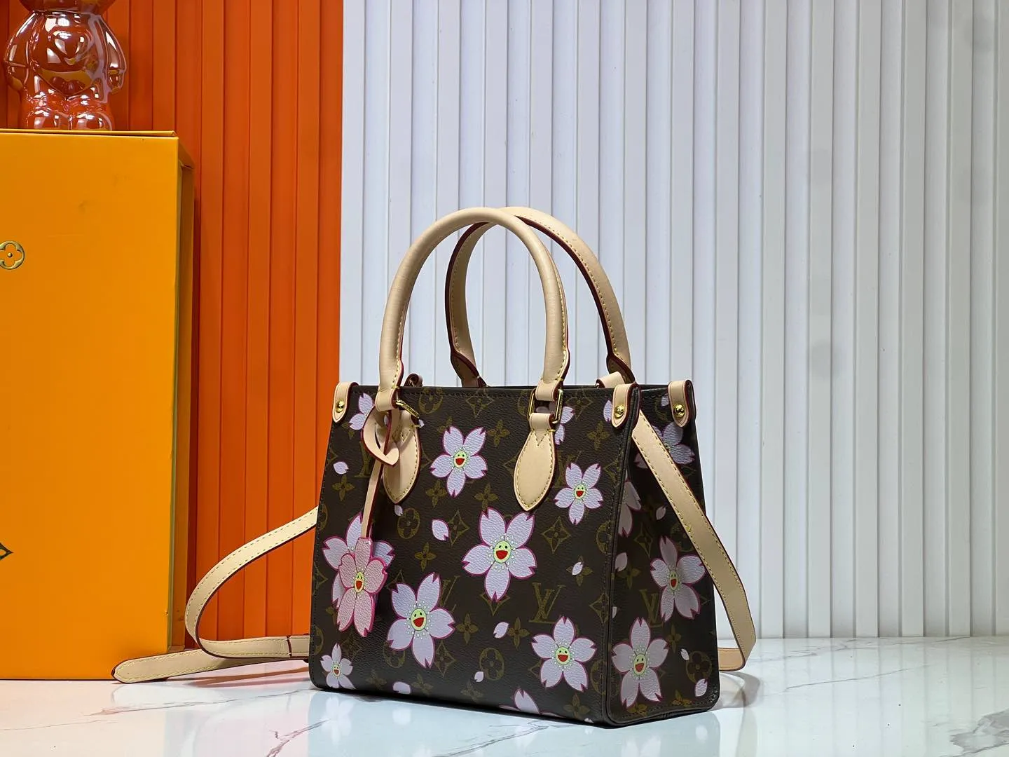 Batch 260💰M45659 M13668!🔥Lv&Takashi Murakami🐼Sakura🌸OnTheGo small new version The legendary ONTHEGO handbag: always able to meet your various needs for handbags. It has a large capacity but is not bulky. It is stiff and soft to the touch, making it suitable for home and travel. Tighten the side ties and it instantly transforms into a stylish urban handbag. Loosen the straps and it transforms into a chic and practical handbag. The slender leather handle can be carried over the shoulder or between the arms. The model shown here is made of Damier Azur canvas. Size: 25x11x19cm