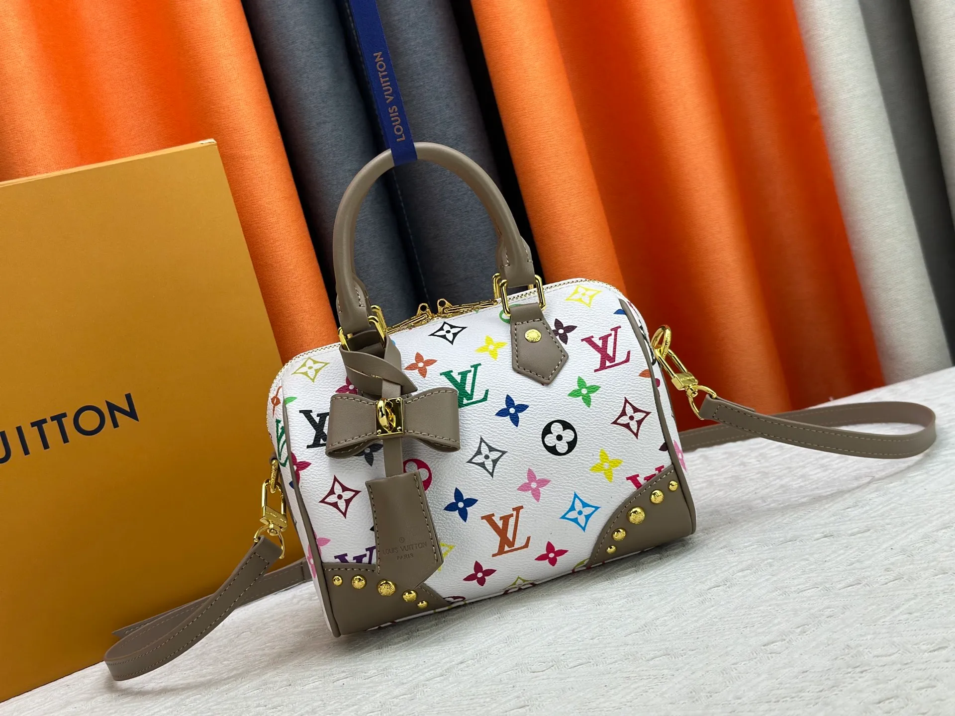 P260 upgraded original M58953 M46234 M46222 Speedy Bandoulière 20 handbag is made of soft coated canvas, and the full-length Monogram pattern is traced in colorful rainbow tones, highlighting the smart style of the Louis Vuitton x Murakami reissue series. The Toron handle and detachable shoulder strap are constructed of cow leather, the metal corners recall classic luggage elements, and the bow-shaped key bag and padlock add brand touches. Dimensions: 20.5 x 13.5 x 12.0 cm (length x height x width)