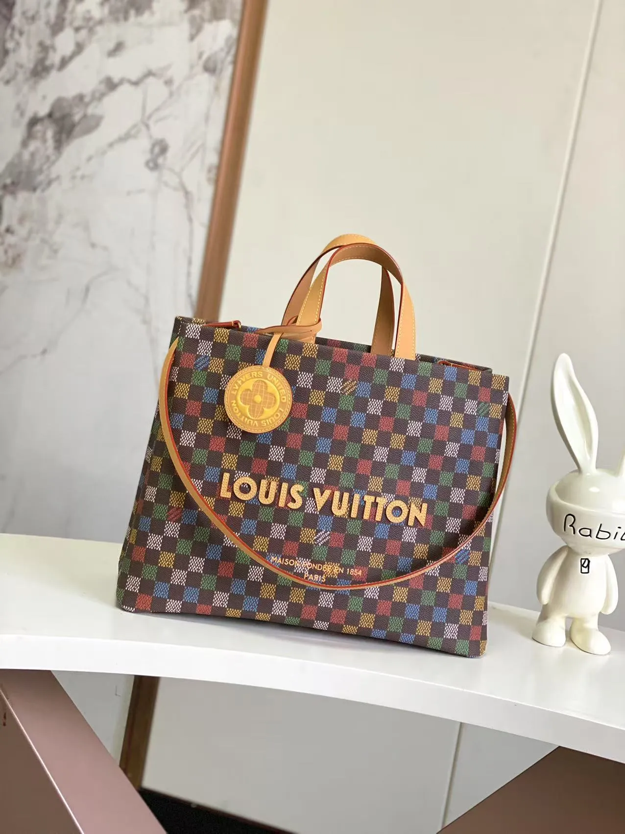 💰1100 Top Original N00192 Shopper Tote handbag design is inspired by Louis Vuitton's classic shopping bag, characterized by the same clean lines and contrasting Louis Vuitton letter logo. Crafted from LVers Damier Ebene coated canvas, this bag features Pharrell Williams' colorful reinterpretation of the Damier pattern (inspired by a classic design created by Georges Vuitton in 1888). Two top handles and a detachable shoulder strap provide a flexible carrying method that combines practicality with unique charm. Dimensions: 32 x 16 x 40 cm