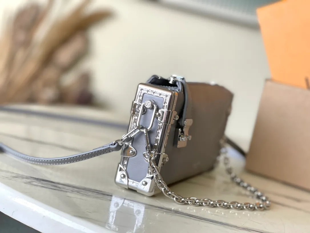 💰1420 (first-grain leather) Top-quality original order M12596 This Slim Trunk handbag draws inspiration from Louis Vuitton’s traditional hard trunk. The soft cow leather is integrated with rivet frames and metal S-lock locks, highlighting the avant-garde rock style. The shiny chain and adjustable leather shoulder strap are both detachable, providing a variety of carrying options. Dimensions: 23 × 12 × 4 cm