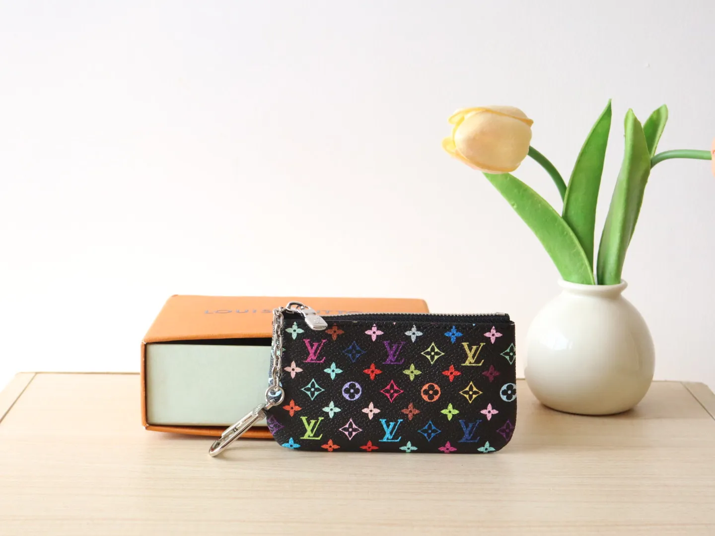 13664 Tricolor Coin Purse🌟P84 This replica Louis Vuitton x Murakami series key coin purse is colorful and made of coated canvas. The vibrant iconic Monogram pattern reinterprets the brand logo with the theme of Japanese artist Takashi Murakami in rainbow tones. The key coin purse has a silver zipper and is equipped with a chain strap and hook buckle to store keys securely. 12 x 7 x 1.5 cm (length x height x width)