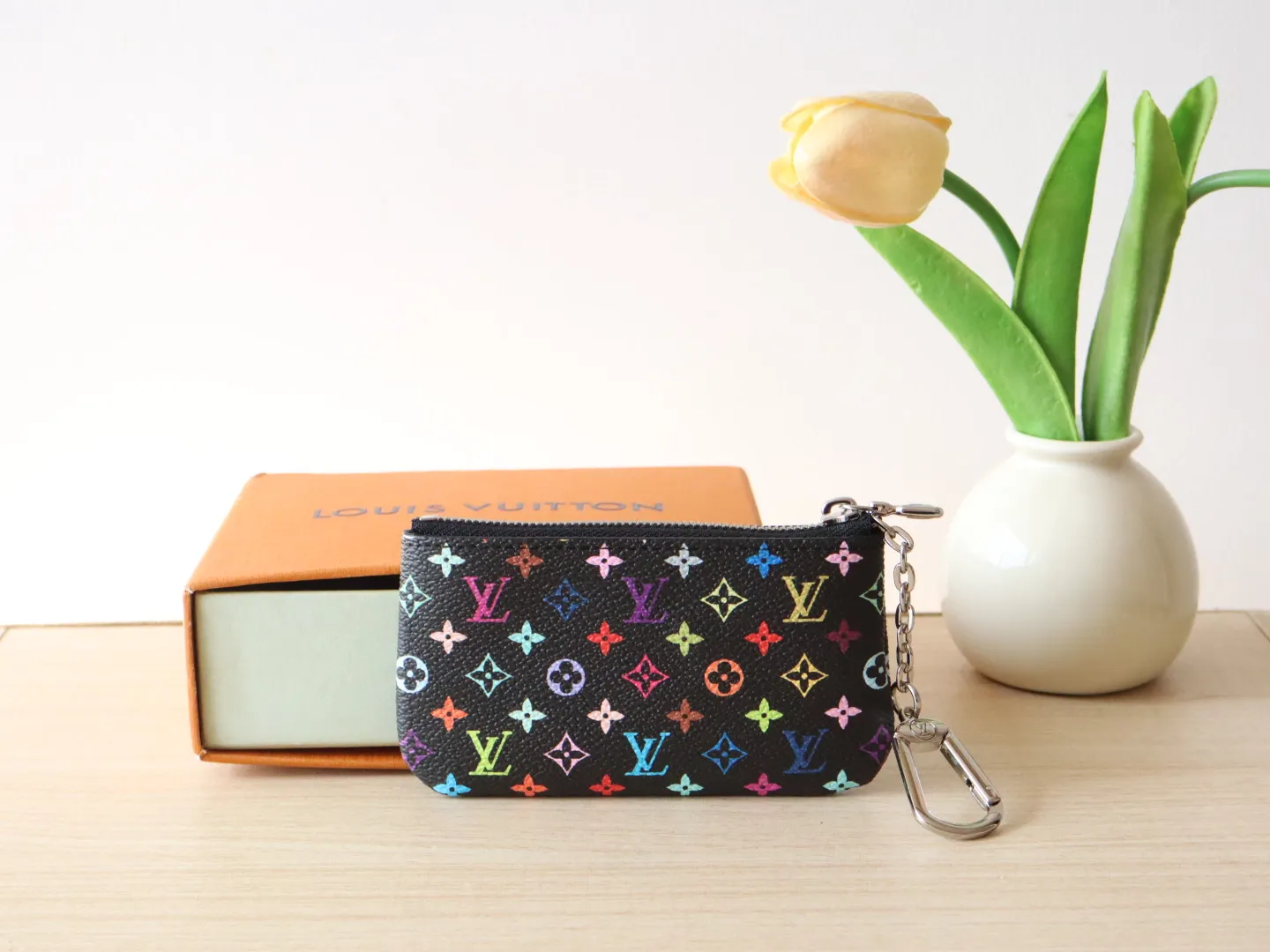 13664 Tricolor Coin Purse🌟P84 This replica Louis Vuitton x Murakami series key coin purse is colorful and made of coated canvas. The vibrant iconic Monogram pattern reinterprets the brand logo with the theme of Japanese artist Takashi Murakami in rainbow tones. The key coin purse has a silver zipper and is equipped with a chain strap and hook buckle to store keys securely. 12 x 7 x 1.5 cm (length x height x width)