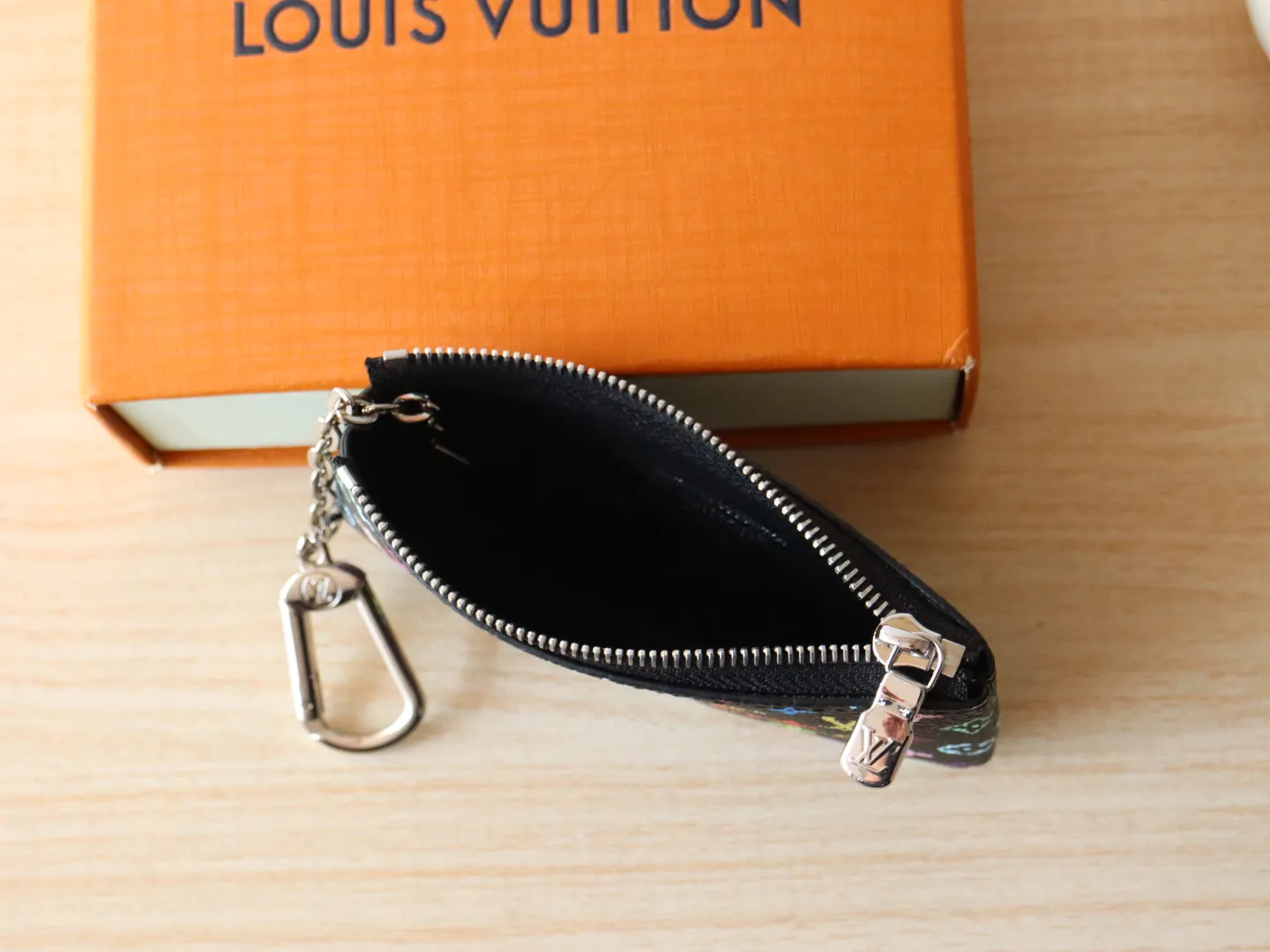 13664 Tricolor Coin Purse🌟P84 This replica Louis Vuitton x Murakami series key coin purse is colorful and made of coated canvas. The vibrant iconic Monogram pattern reinterprets the brand logo with the theme of Japanese artist Takashi Murakami in rainbow tones. The key coin purse has a silver zipper and is equipped with a chain strap and hook buckle to store keys securely. 12 x 7 x 1.5 cm (length x height x width)