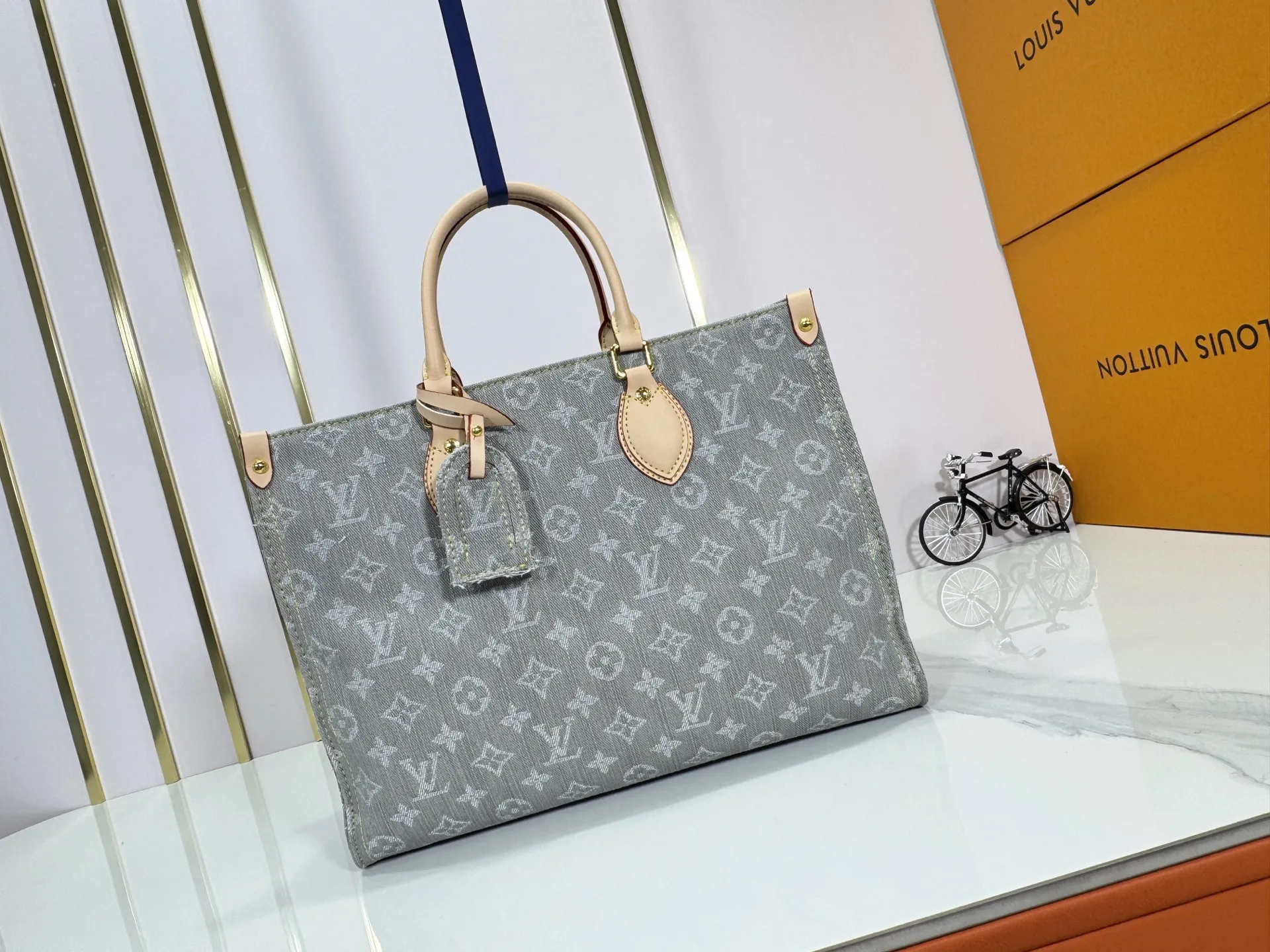 P320 M49495 M45659 M13189 New Gray Denim Denim This edition of OnTheGo MM celebrates the return of the iconic Monogram denim pattern in 2005. It's made from organic cotton, artfully woven with black and white threads and then bleached using a special Louis Vuitton technique to create a vintage-inspired finish. It's sized to hold a laptop, features light gold hardware, and includes signature details like natural leather accents and a removable name tag. Dimensions: 35 x 27 x 14 cm