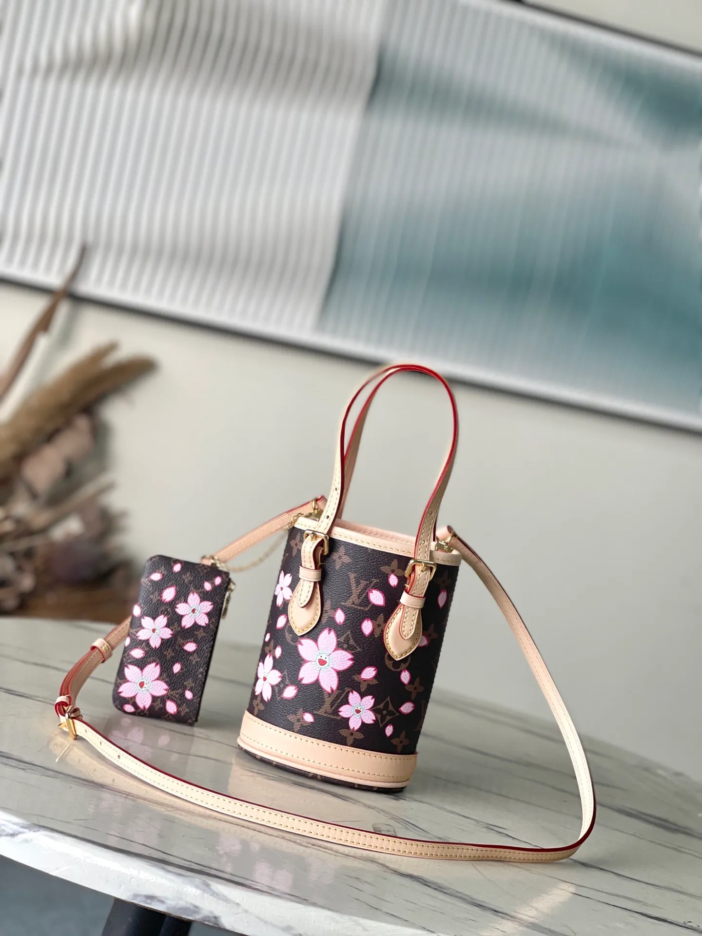 💰900 Top Original Order M13417 This Nano Bucket handbag is made of classic Monogram coated canvas and has a sophisticated design, with cow leather trim and dazzling metal parts to complete the whole. The Cherry Blossom pattern on the body of the bag conveys the atmosphere of prosperous recovery and highlights the distinctive style of Japanese artist Takashi Murakami. The detachable shoulder strap allows for a variety of carrying options, and the leather keychain adds a functional detail. Dimensions: 13 × 17 × 9 cm