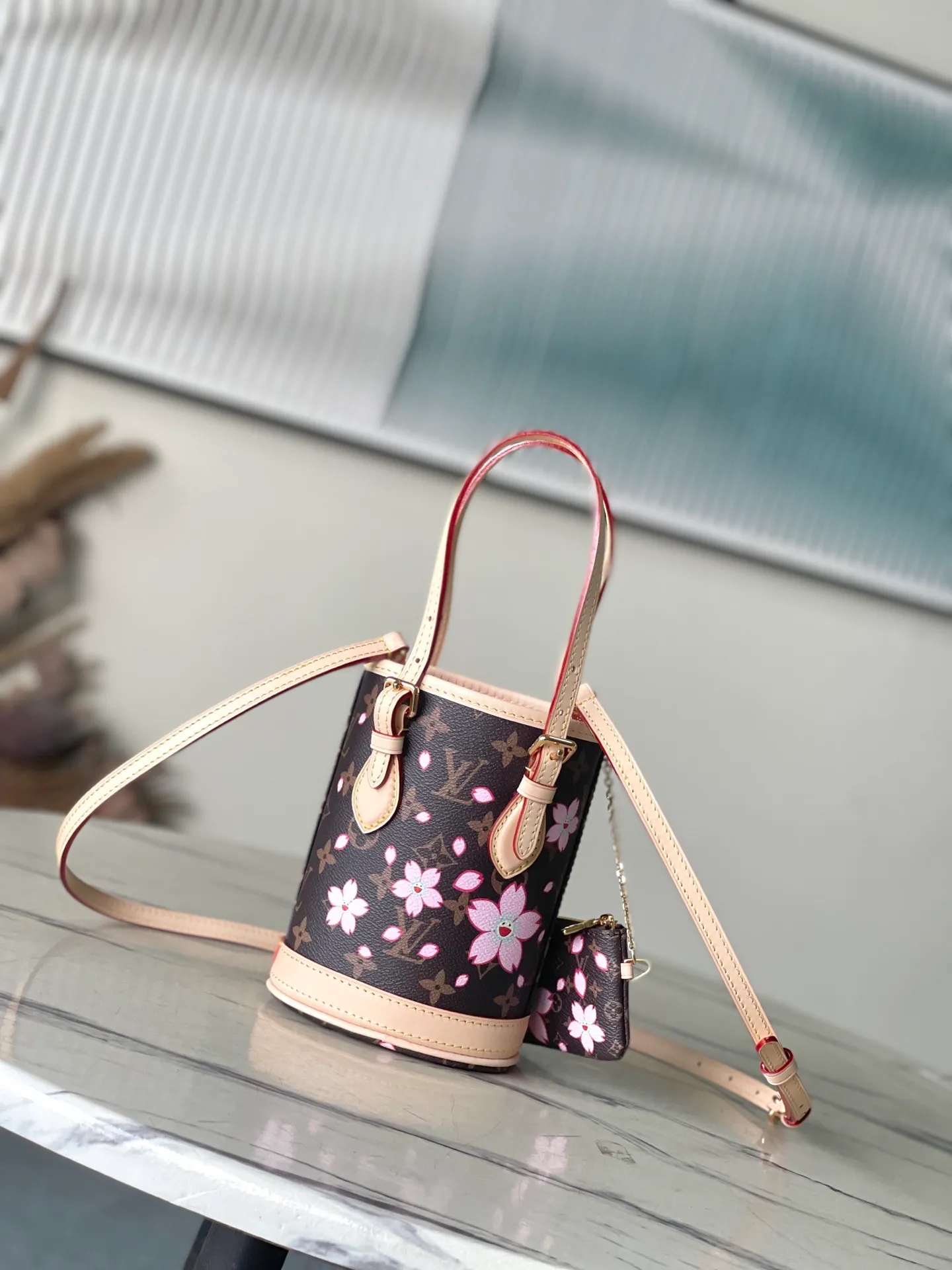 💰900 Top Original Order M13417 This Nano Bucket handbag is made of classic Monogram coated canvas and has a sophisticated design, with cow leather trim and dazzling metal parts to complete the whole. The Cherry Blossom pattern on the body of the bag conveys the atmosphere of prosperous recovery and highlights the distinctive style of Japanese artist Takashi Murakami. The detachable shoulder strap allows for a variety of carrying options, and the leather keychain adds a functional detail. Dimensions: 13 × 17 × 9 cm