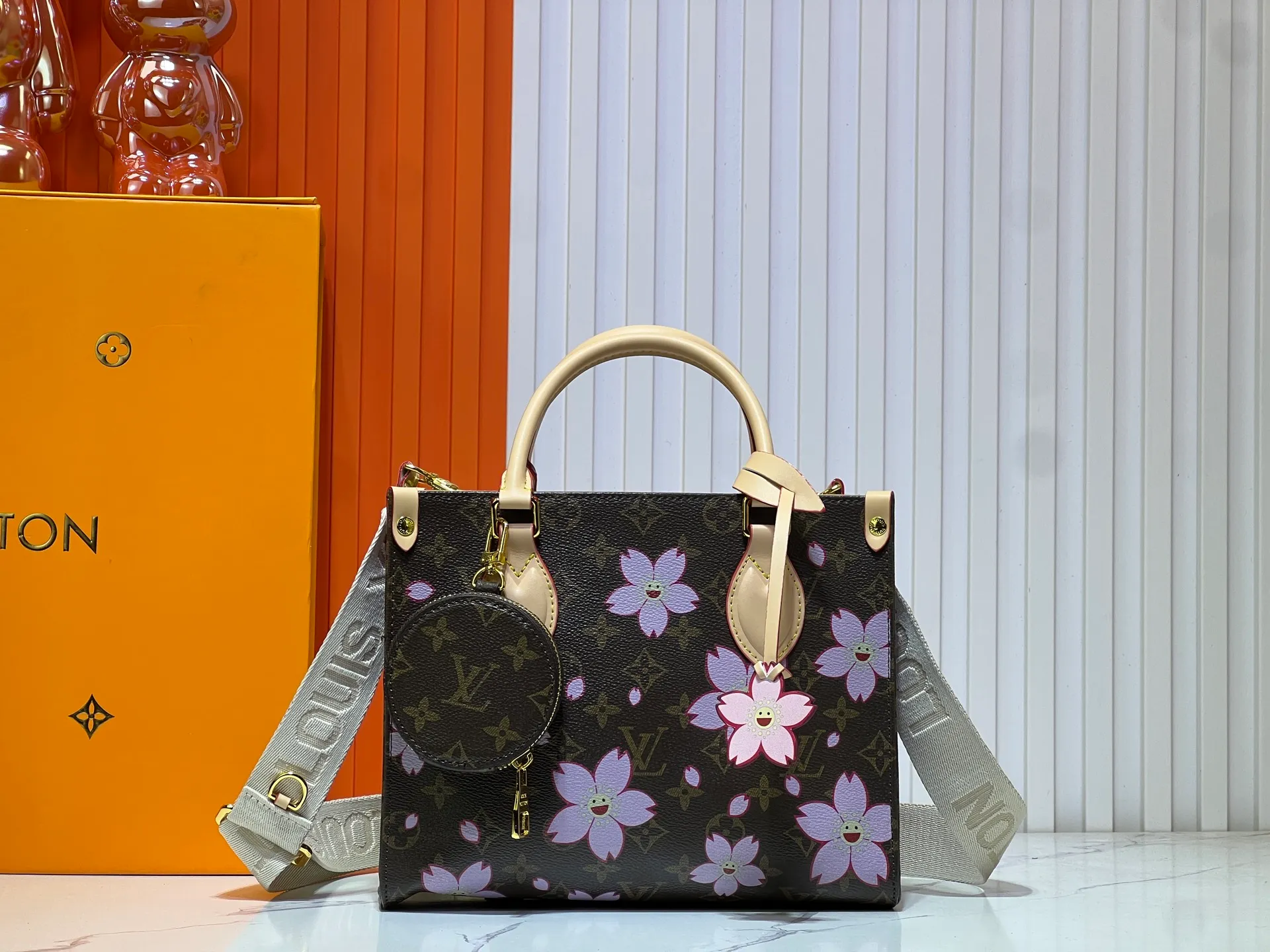 Batch 320💰M45659 M46373🔥Lv&Takashi Murakami🐼Sakura🌸OnTheGo small new version The legendary ONTHEGO handbag: always able to meet your various needs for handbags. It has a large capacity but is not bulky. It is stiff and soft to the touch, making it suitable for home and travel. Tighten the side ties and it instantly transforms into a stylish urban handbag. Loosen the straps and it transforms into a chic and practical handbag. The slender leather handle can be carried over the shoulder or between the arms. The model shown here is made of Damier Azur canvas. Size: 25x11x19cm
