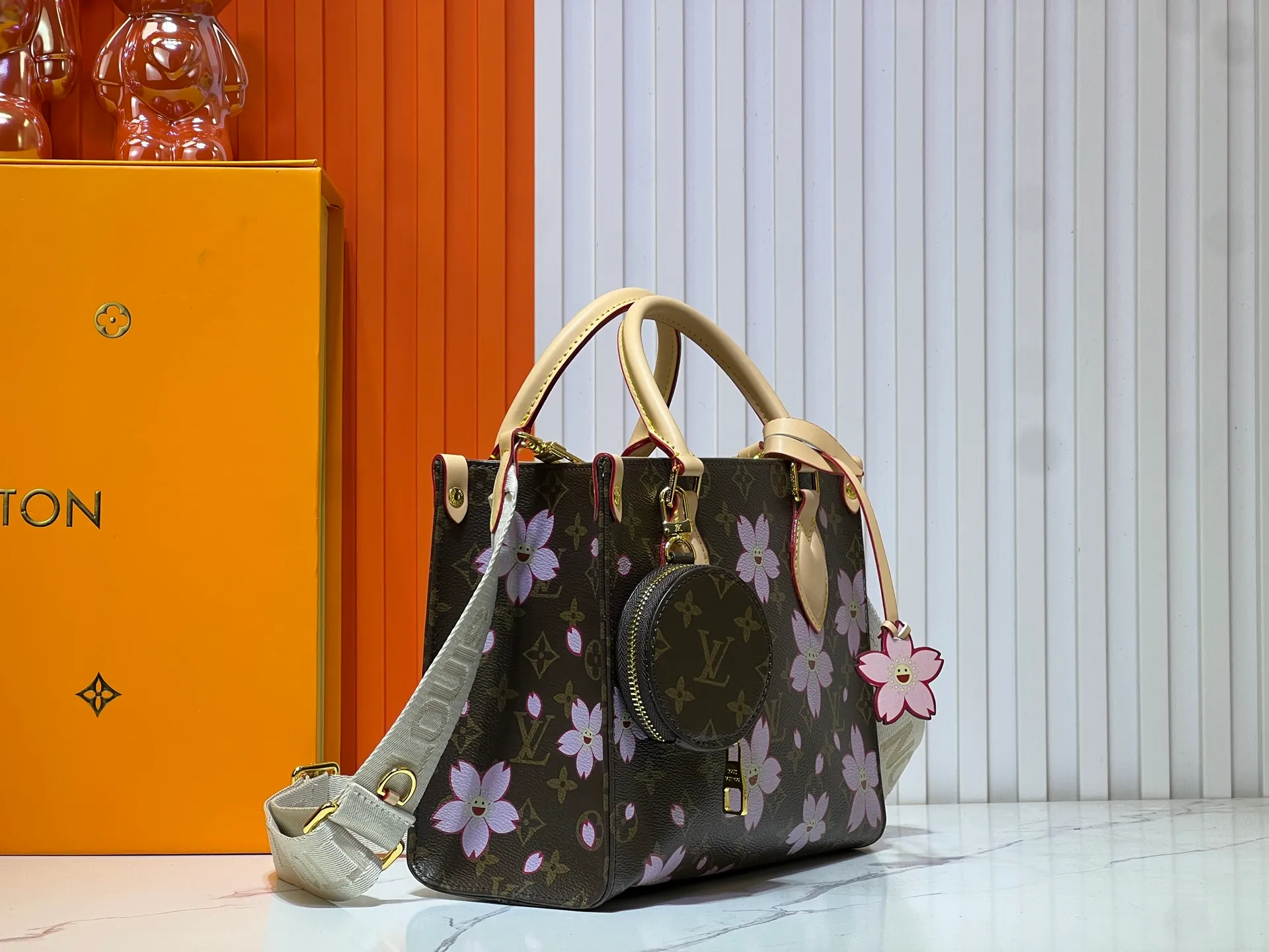 Batch 320💰M45659 M46373🔥Lv&Takashi Murakami🐼Sakura🌸OnTheGo small new version The legendary ONTHEGO handbag: always able to meet your various needs for handbags. It has a large capacity but is not bulky. It is stiff and soft to the touch, making it suitable for home and travel. Tighten the side ties and it instantly transforms into a stylish urban handbag. Loosen the straps and it transforms into a chic and practical handbag. The slender leather handle can be carried over the shoulder or between the arms. The model shown here is made of Damier Azur canvas. Size: 25x11x19cm