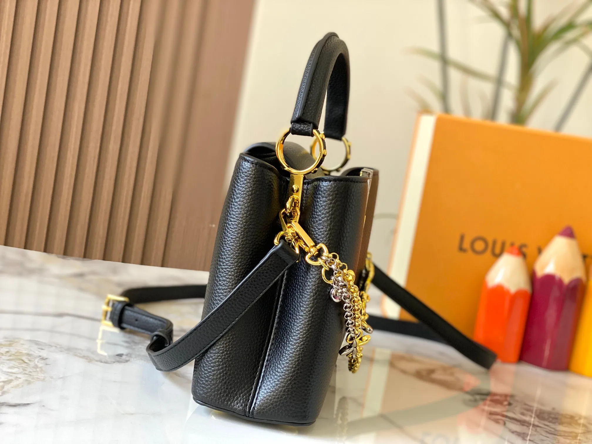 P500 [Guangzhou top quality original version] M26532 black gold. This modern version of Capucines BB is made of timeless Taurillon leather and equipped with a jewelry-inspired Infinity chain. The bag is decorated with double galvanized metal parts, including the iconic Monogram floral pattern, and the LV Initials logo created with sunburst technology, creating a sundial-like light and shadow effect. The bag has multiple pockets and a detachable shoulder strap, allowing it to be carried on one shoulder or across the body. 27 x 17.3 x 9 (cm) (length x height x width)
