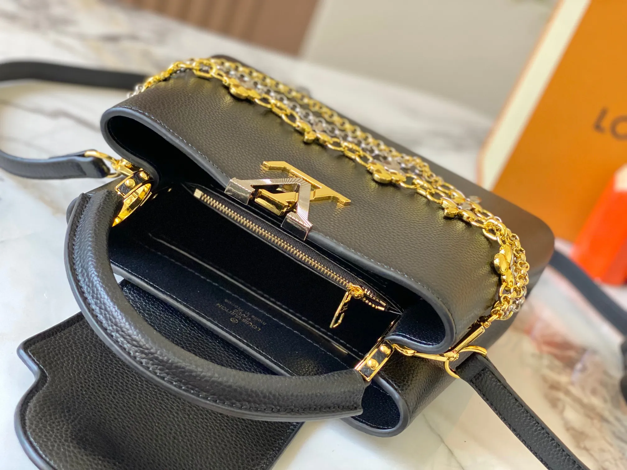 P500 [Guangzhou top quality original version] M26532 black gold. This modern version of Capucines BB is made of timeless Taurillon leather and equipped with a jewelry-inspired Infinity chain. The bag is decorated with double galvanized metal parts, including the iconic Monogram floral pattern, and the LV Initials logo created with sunburst technology, creating a sundial-like light and shadow effect. The bag has multiple pockets and a detachable shoulder strap, allowing it to be carried on one shoulder or across the body. 27 x 17.3 x 9 (cm) (length x height x width)