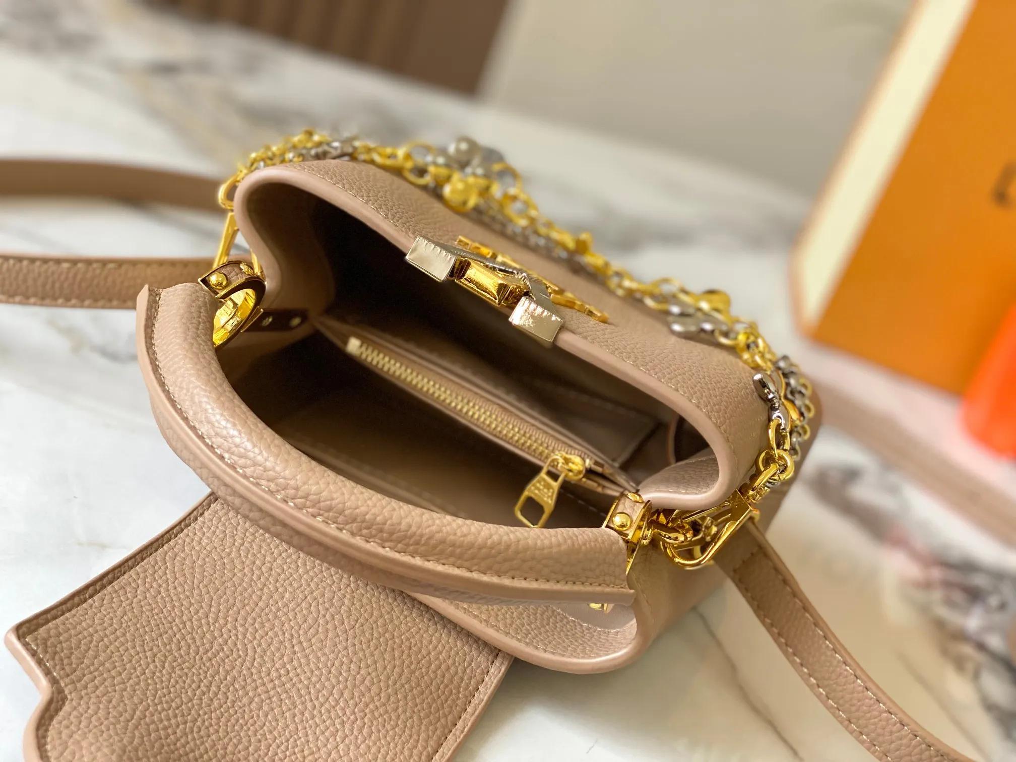 P480 [Guangzhou top quality original version] M26351 apricot color. This modern version of the Capucines mini is made of timeless Taurillon leather and equipped with a jewelry-inspired Infinity chain. The bag is decorated with double galvanized metal parts, including the iconic Monogram floral pattern, and the LV Initials logo created with sunburst technology, creating a sundial-like light and shadow effect. The bag has multiple pockets and a detachable shoulder strap, allowing it to be carried on one shoulder or across the body. 14 x 8 x 21 cm (height x width x length)