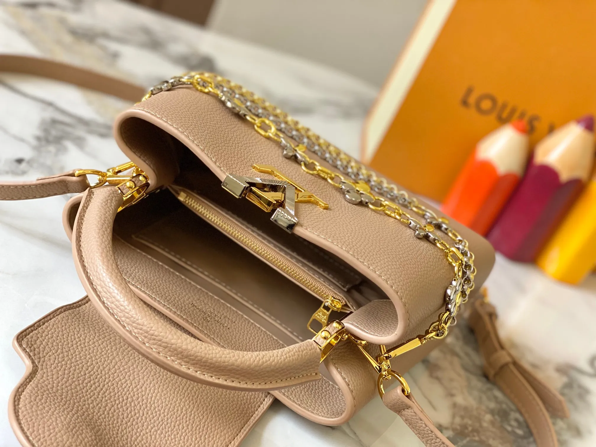 P500 [Guangzhou top quality original version] M26532 apricot color. This modern version of Capucines BB is made of timeless Taurillon leather and equipped with a jewelry-inspired Infinity chain. The bag is decorated with double galvanized metal parts, including the iconic Monogram floral pattern, and the LV Initials logo created with sunburst technology, creating a sundial-like light and shadow effect. The bag has multiple pockets and a detachable shoulder strap, allowing it to be carried on one shoulder or across the body. 27 x 17.3 x 9 (cm) (length x height x width)