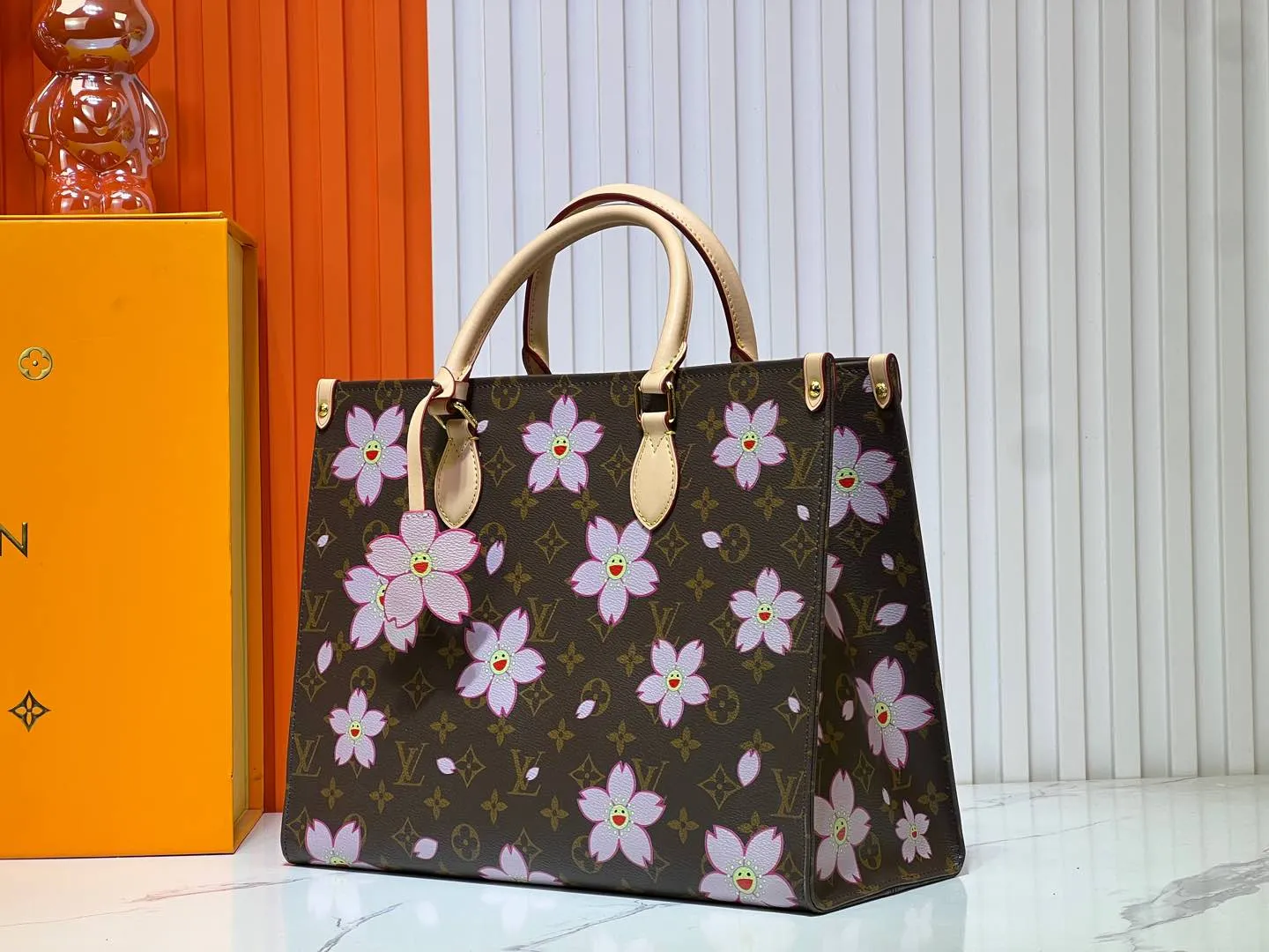 Batch 280💰M45039 M13668!🔥Lv&Takashi Murakami Sakura🌸OnTheGo new version The legendary ONTHEGO handbag: always able to meet your various needs for handbags. It has a large capacity but is not bulky. It is stiff and soft to the touch, making it suitable for home and travel. Tighten the side ties and it instantly transforms into a stylish urban handbag. Loosen the straps and it transforms into a chic and practical handbag. The slender leather handle can be carried over the shoulder or between the arms. The model shown here is made of Damier Azur canvas. Size: 35x27x14cm