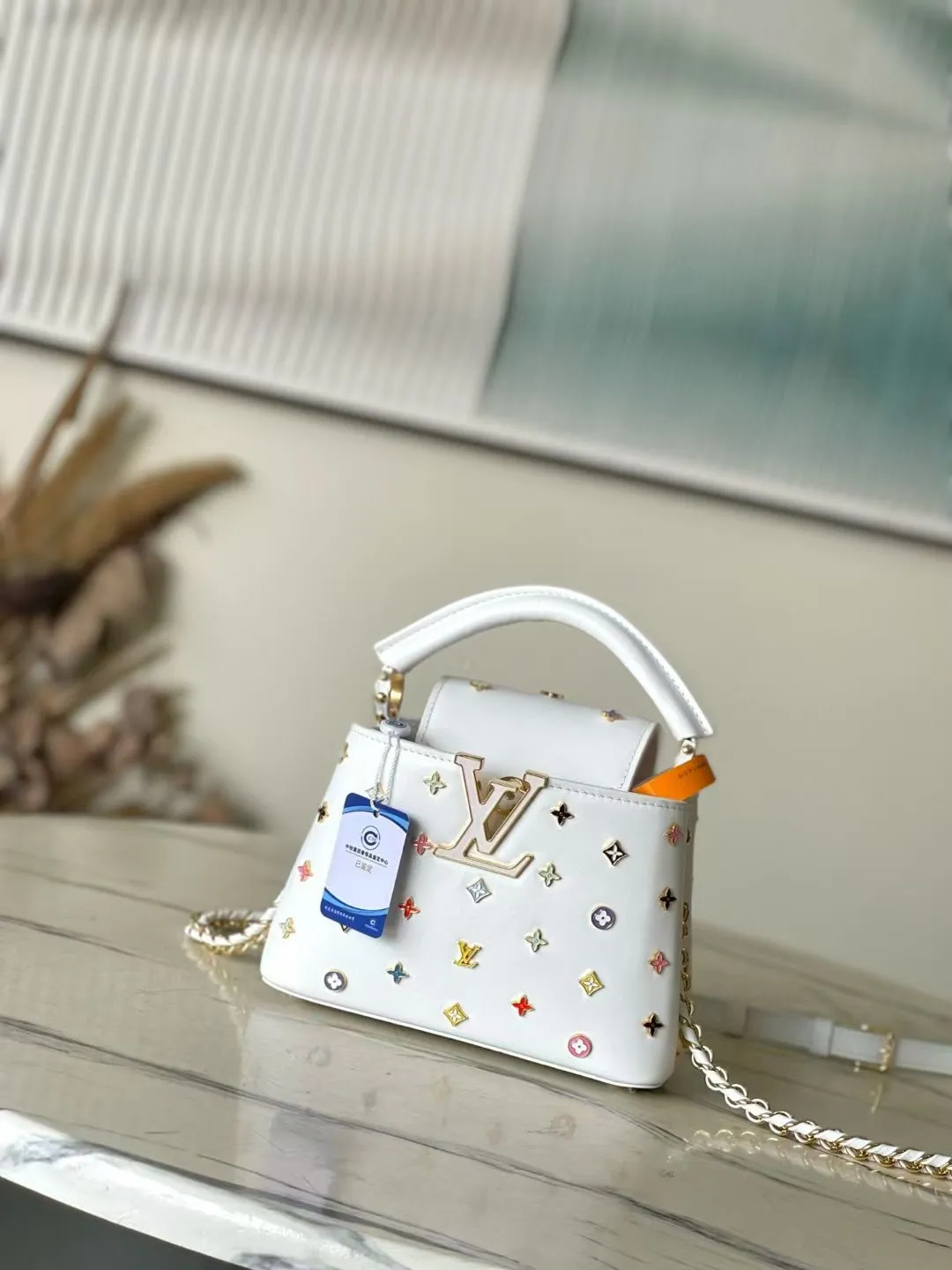 💰2740 "Special Original Leather" M14165 White This Capucines handbag is from the Louis Vuitton x Murakami reissue series, using Taurillon cow leather to interpret the classic design in a fun way. The LV lettering and detachable Monogram strap are dipped in bright hues, a nod to the artist's signature iridescent brushwork. The bow-shaped key holder and padlock decoration add sophisticated details, and the interior compartments and multiple pockets can easily store your daily needs. 21.0 x 13.5 x 8.0 cm (L x H x W) • Taurillon cow leather • Cow leather trim • Cow leather lining • Metal hardware • Flap can be placed on the inside or outside • Internal compartment • Internal zip pocket • Internal patch pocket • Key holder • Padlock • Metal base stud