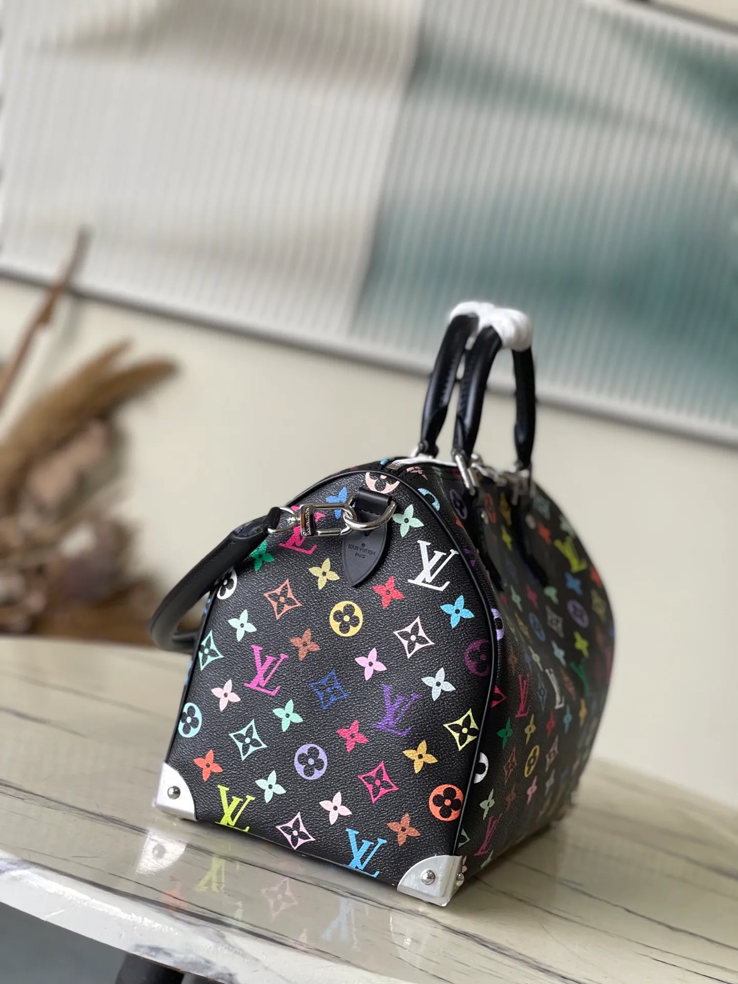 💰1180 Top Original M13257 This SpeedySoft 30 handbag is made of soft coated canvas, and the full-length Monogram pattern is traced in colorful rainbow tones, highlighting the smart style of the x Murakami Takashi reissue series. The Toron handle and detachable shoulder strap are constructed of cow leather, the metal corners recall classic luggage elements, and the bow-shaped key bag and padlock add brand touches. Dimensions: 30 × 21 × 17 cm