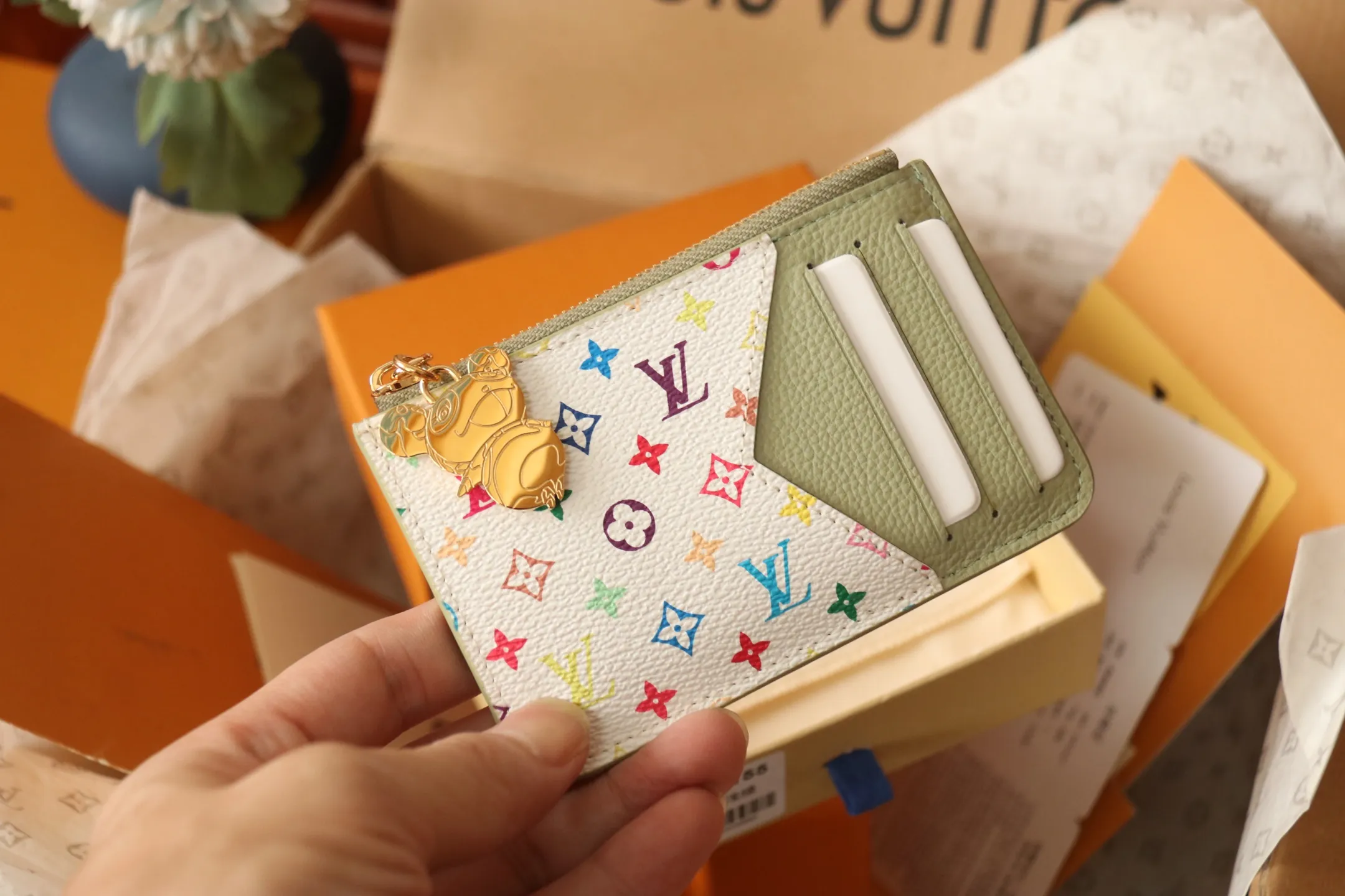 【LV x TM Romy Card Holder】 💎p400 m14155 rose m14171 blue m13800 green "LV × TM Porto Kurt Romy" appears in the "Louis Vuitton × Takashi Murakami" series that unfolds in a variety of categories. It features functional and playful expressions with fresh tones inspired by the rainbow colors unique to Japanese artists. The whole piece is finished with Monogram Amplant leather that adds a casual personality, and the bright Monogram multi-color canvas in the flat pocket stands out. The coin pocket opens and closes with a gold zipper and features a panda pull to symbolize the season.  Dimensions: 12 x 8 x 0.8 cm