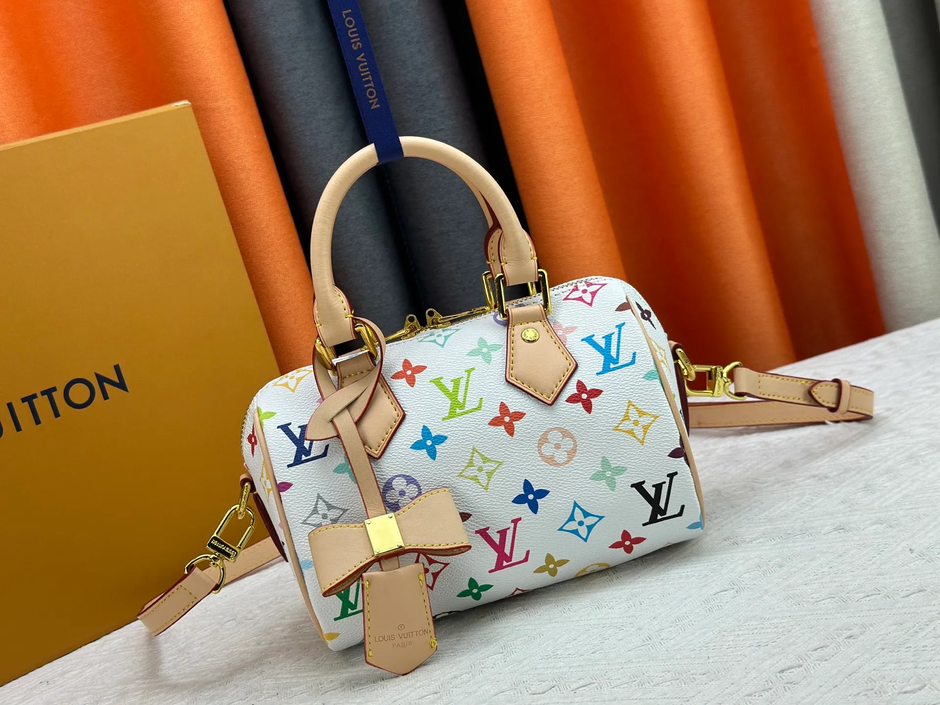 P260 Upgraded from the original version, this M46234 M46222 Speedy Bandoulière 20 handbag is made of soft coated canvas, with the full-length Monogram pattern traced in colorful rainbow tones, highlighting the smart style of the Louis Vuitton x Murakami reissue series. The Toron handle and detachable shoulder strap are constructed of cow leather, the metal corners recall classic luggage elements, and the bow-shaped key bag and padlock add brand touches. Dimensions: 20.5 x 13.5 x 12.0 cm (length x height x width)