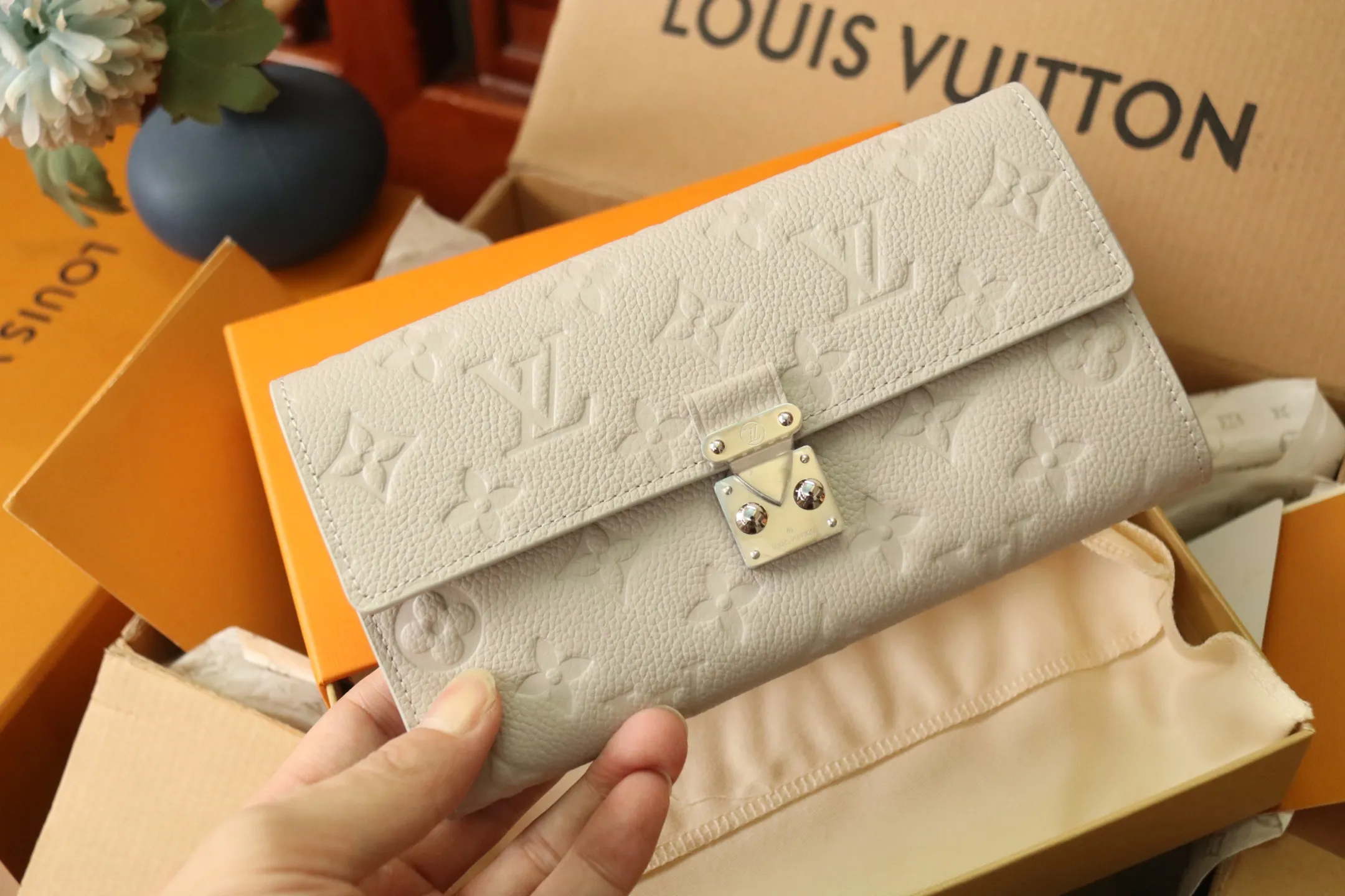 M13463 Gray 🌟 "Portefeuille Sara Metis" in P600 leather. The flaps are decorated with golden S-lock style buttons inspired by Louis Vuitton’s traditional trunks that symbolize “Métis”. It features an elegant rectangular shape and multiple pockets, as well as a spacious interior with compartments and card slots.  19 x 11 x 3cm