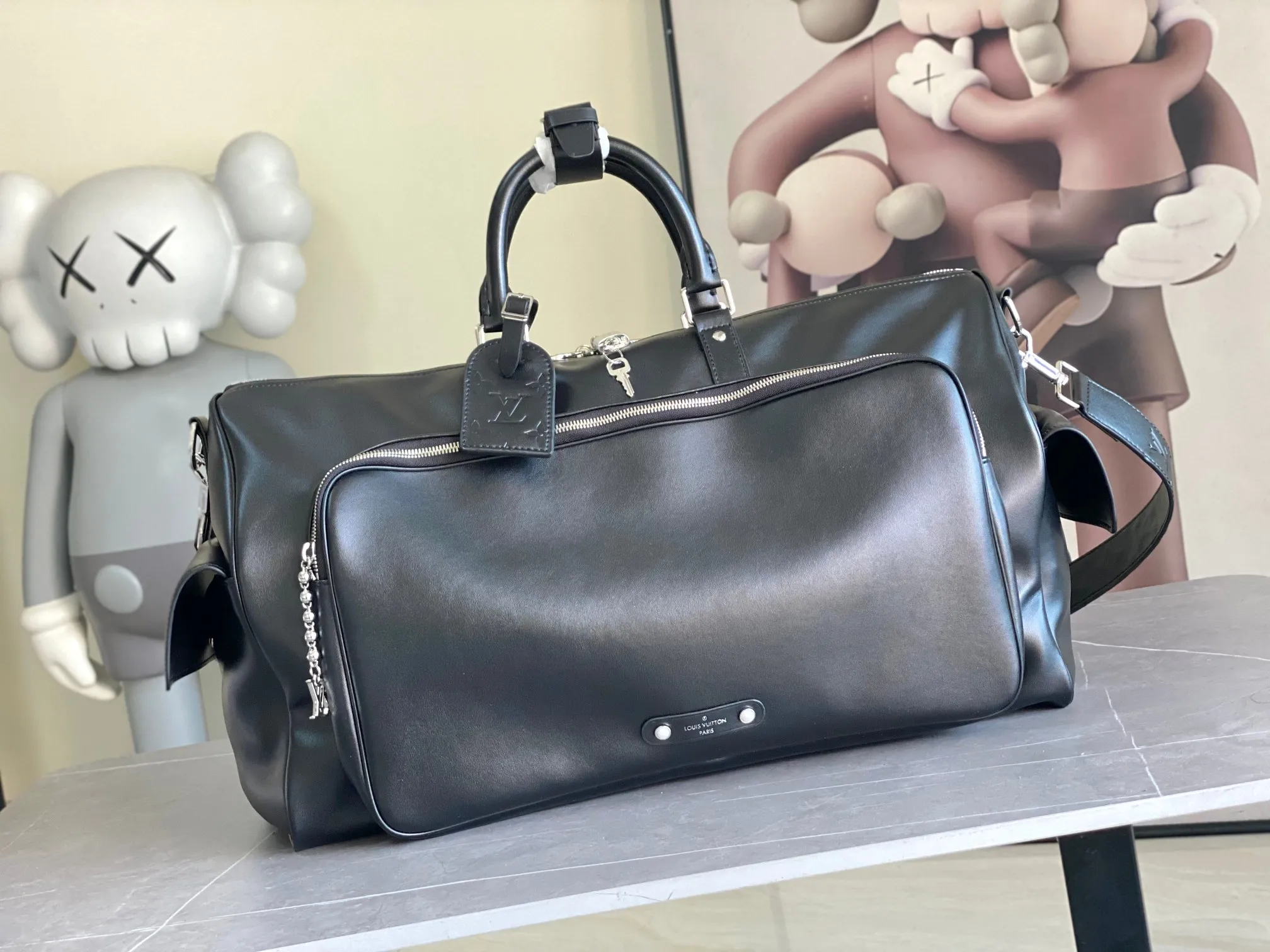 💰1760 (top layer leather) top original order M13992 This Keepall Bandoulière 50 travel bag depicts the Monogram pattern on the canvas surface and transforms into a cartoon image, making the Monogram flowers and LV letters present rich emotions of sadness or joy. The top handle and side straps are made of leather, continuing the consistent design of the Keepall series. Cartoon name tags can be customized. size：50x29x23cm