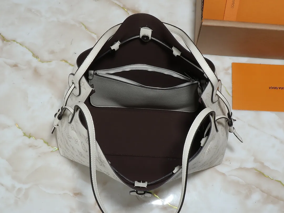 💰280💰Upgraded from the original M13180 Mahina series introduces the Boundless handbag - a multi-functional daily design. It's made from House's signature perforated Mahina leather and is roomy enough to store essential items, including a laptop and tablet. The shoulder bag features a removable zip pocket and is embellished with silver hardware for a sophisticated look. Dimensions: 16.9 x 13.2 x 6.7 inches (LxHxW)
