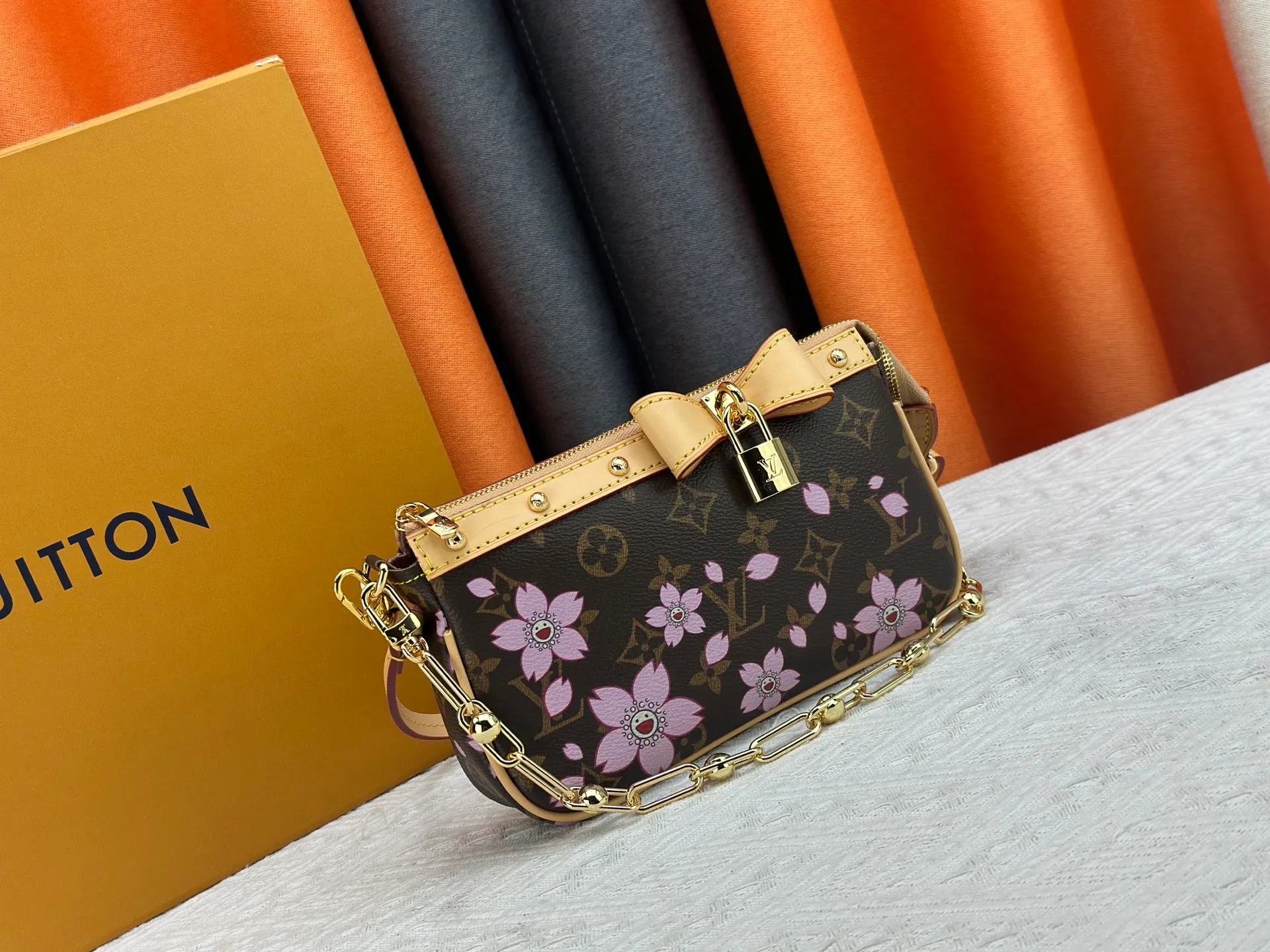 P240 M13666 This Pochette Accessoires handbag is made of classic Monogram canvas with the bright Cherry Blossom pattern written by Takashi Murakami, which brings out the distinctive elements of the Louis Vuitton x Takashi Murakami replica series in a playful style. A leather bow and LV-engraved padlock accentuate the upper edge, while dazzling studs and a detachable chain add a touch of uninhibited style. Monogram coated canvas leather trimmed fabric lining with metal hardware, zipper closure, can store a 6.7-inch smartphone and card holder. The shoulder strap is removable and not adjustable. Size: 22x13x4cm