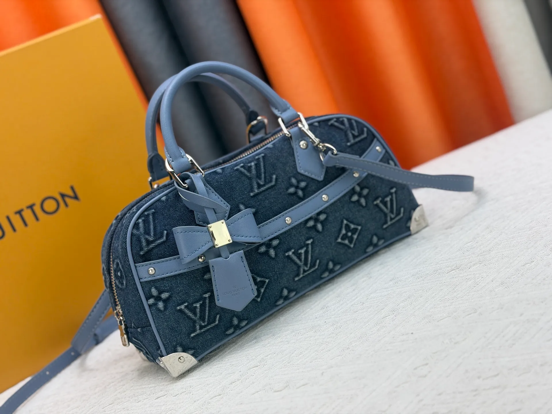 P360 M13084 Embossed Denim This Handbag East West handbag is from the Louis Vuitton x Takashi Murakami reissue series, using the artist's signature rainbow tones to trace the full-length Monogram pattern. Sleek horizontal construction lines the top handle, studded side straps, detachable and adjustable shoulder strap and LV x TM key holder, with cowhide leather details and sophisticated corners that nod to the brand's traditional luggage.  14 x 10 x 27 cm (H x W x L) Monogram coated canvas Cow leather trim Textile lining Metal hardware Zip closure Internal pocket Holds smartphone, keys, headphones and Zippy wallet Shoulder strap: removable, not adjustable Strap half-length: 44.0 cm Handle: Double handle