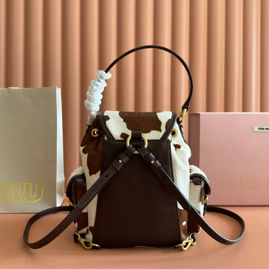 p1900💋💋💋【Original leather configuration counter complete package】𝐌𝐈𝐔𝐌𝐈𝐔 New cow pattern backpack Miu Miu's cow pattern backpack perfectly combines retro wildness and girly sweetness. The brown and white contrasting cow pattern fur material comes with an eye-catching buff, and is matched with the iconic logo embossing, showing the brand style in every detail; the drawstring flap design combines practicality with retro charm, and the combination of leather handles and shoulder straps, 🉑hand-held🉑shoulder-carrying, easily adapts to different wearing scenarios. Whether paired with casual denim or a sweet girl-style skirt, it can instantly inject a personal touch into the look and is the finishing touch to unlock niche fashion. Style number: 5B043 Small size: bottom length 23x height 25x width 13cm