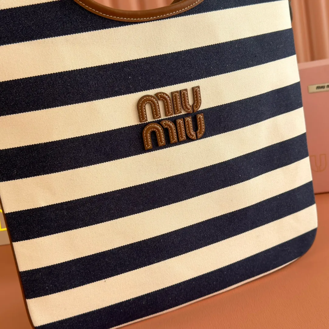 p1300. 💋💋💋【Full set of packages at the counter】𝗠𝗜𝗨𝗠𝗜𝗨 𝗙𝗪𝟮𝟱 𝗡𝗲𝘄 𝗮𝗿𝗿𝗶𝘃𝗮𝗹!      When striped canvas meets hobo's lazy gene, it grabs the first wave in autumn and winter. The relaxed feeling of commuting is directly capped. Classic blue and white nautical striped canvas × Italian calfskin piping. Flexible bag body hangs naturally. Tote capacity + Hobo's lazy feeling two-in-one. It looked like it was 𝗷𝗮𝗰𝗸𝗲𝘁 canvas, but when I touched the edge of the leather, I realized it was 𝗹𝘂𝘅𝘂𝗿𝘆!   The Ju Neng suit still hasn’t collapsed! 𝗵𝗼𝗯𝗼Bag shape looks slim 𝟭𝟬𝟬% 5BG231 stripes Size: 35×40cm
