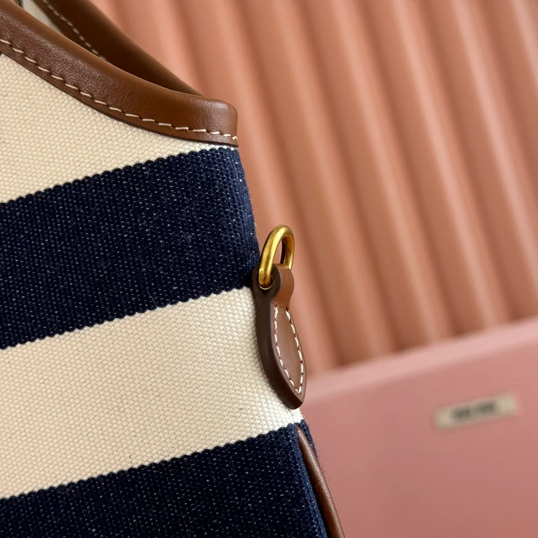 p1300. 💋💋💋【Full set of packages at the counter】𝗠𝗜𝗨𝗠𝗜𝗨 𝗙𝗪𝟮𝟱 𝗡𝗲𝘄 𝗮𝗿𝗿𝗶𝘃𝗮𝗹!      When striped canvas meets hobo's lazy gene, it grabs the first wave in autumn and winter. The relaxed feeling of commuting is directly capped. Classic blue and white nautical striped canvas × Italian calfskin piping. Flexible bag body hangs naturally. Tote capacity + Hobo's lazy feeling two-in-one. It looked like it was 𝗷𝗮𝗰𝗸𝗲𝘁 canvas, but when I touched the edge of the leather, I realized it was 𝗹𝘂𝘅𝘂𝗿𝘆!   The Ju Neng suit still hasn’t collapsed! 𝗵𝗼𝗯𝗼Bag shape looks slim 𝟭𝟬𝟬% 5BG231 stripes Size: 35×40cm