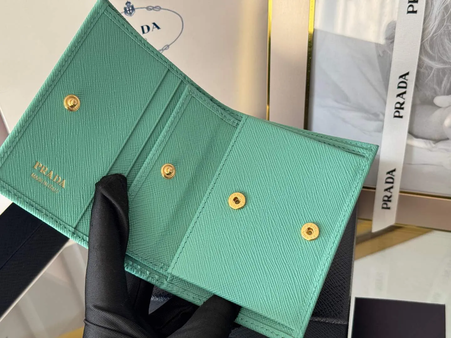 Prada women's two-fold short clip, with coin pocket and coin pocket. Model 1M0204, cross-grain cowhide. Size: 11.2x9.5cm. Simple and practical to enhance personal taste.