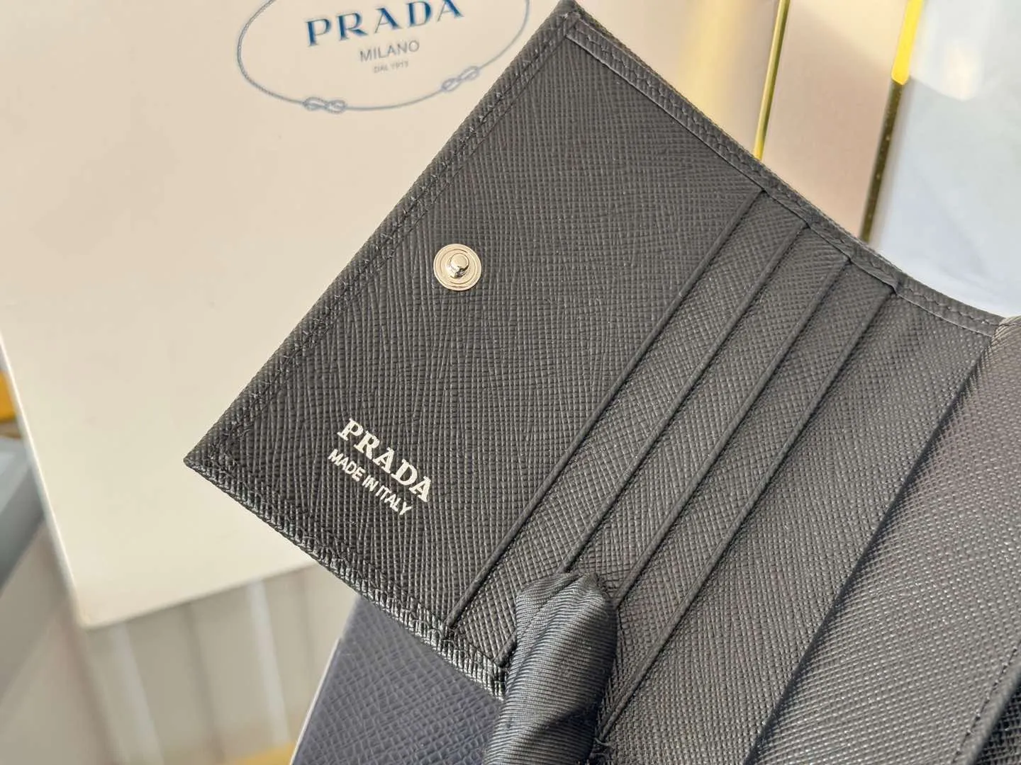 Prada women's two-fold short clip, with coin pocket and coin pocket. Model 1M0204, cross-grain cowhide. Size: 11.2x9.5cm. Simple and practical to enhance personal taste.