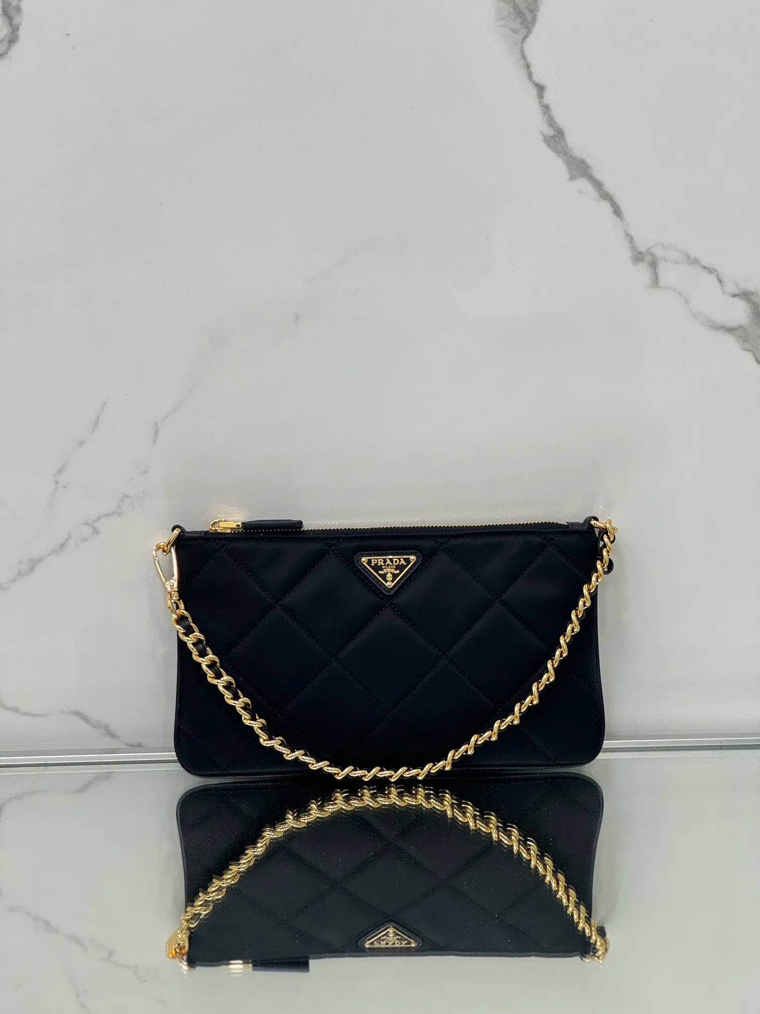 💰700🌟Chain Underarm Bag This clutch bag is made of regenerated nylon (Re-Nylon), which reflects the sustainable evolution of Prada's iconic fabric and adopts a simple and elegant design. Embodying the duality at the core of the brand, it cleverly blends modern and practical regenerated nylon with charming and refined details. It features chain handles, tonal stitching and the signature enameled triangle metal logo. Size: 24.5×14cm Style number: 1NI054