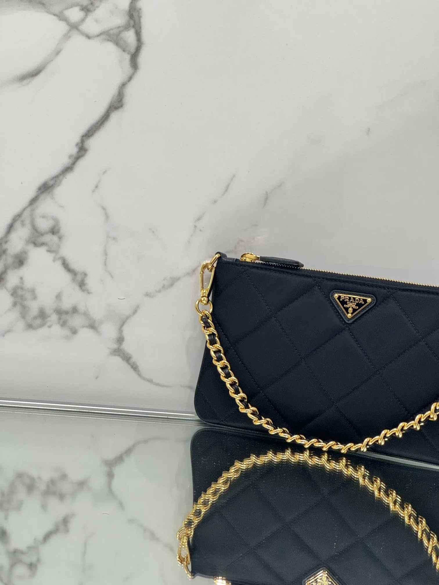 💰700🌟Chain Underarm Bag This clutch bag is made of regenerated nylon (Re-Nylon), which reflects the sustainable evolution of Prada's iconic fabric and adopts a simple and elegant design. Embodying the duality at the core of the brand, it cleverly blends modern and practical regenerated nylon with charming and refined details. It features chain handles, tonal stitching and the signature enameled triangle metal logo. Size: 24.5×14cm Style number: 1NI054