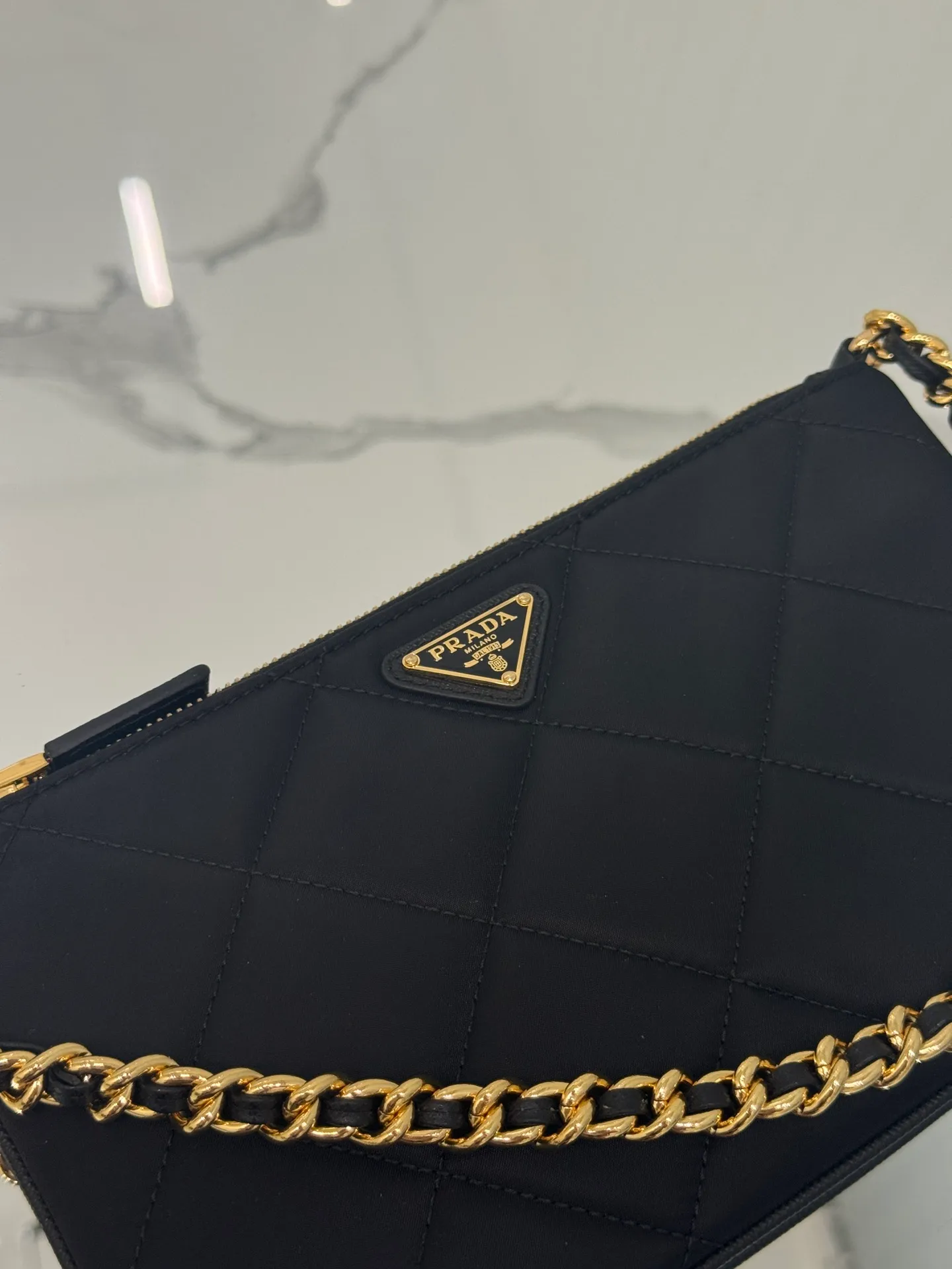 💰700🌟Chain Underarm Bag This clutch bag is made of regenerated nylon (Re-Nylon), which reflects the sustainable evolution of Prada's iconic fabric and adopts a simple and elegant design. Embodying the duality at the core of the brand, it cleverly blends modern and practical regenerated nylon with charming and refined details. It features chain handles, tonal stitching and the signature enameled triangle metal logo. Size: 24.5×14cm Style number: 1NI054