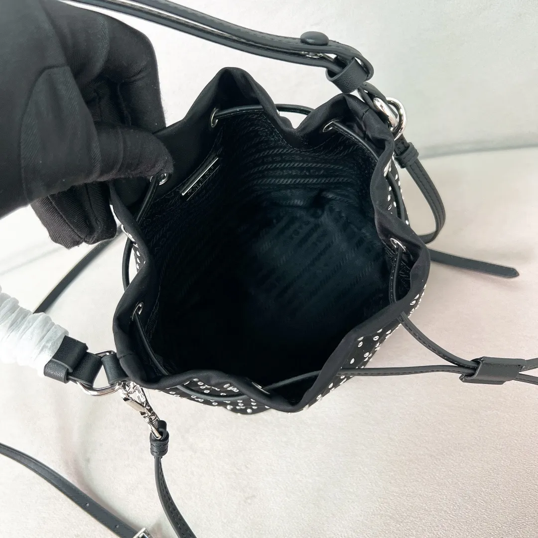 💰1140✨New product debut✨2025 new rivet decoration series bucket bag 1BE067 Imported recycled nylon fabric with rivet decoration Classic triangle logo Drawstring fastening design You can adjust the space at will Lightweight can be loaded and easy to match The randomness of different carrying methods and the ease of putting it anywhere Transform into a stylish girl in seconds🤩 Size：19.5/15.5/10