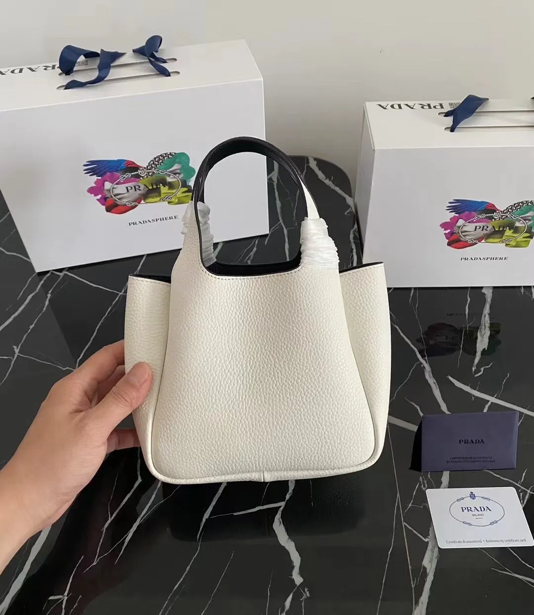 P1100¥ [Top original order] The latest 2022 vegetable basket tote bag mini model 1BA349 has arrived🎉🎉Soft and delicate pebbled calfskin tote bag, full leather inside and outside, equipped with double handles, decorated with silver metal logo, the overall body of the bag is very soft Lightweight, elegant and outstanding. The two side pockets not only meet the needs of exquisite storage but also add an elegant charm. It can be carried as a handbag or an armpit bag. It is a must-have handbag for fairies that perfectly combines classic heritage with the trend of the times. Size: 18︸15.5︸10CM!