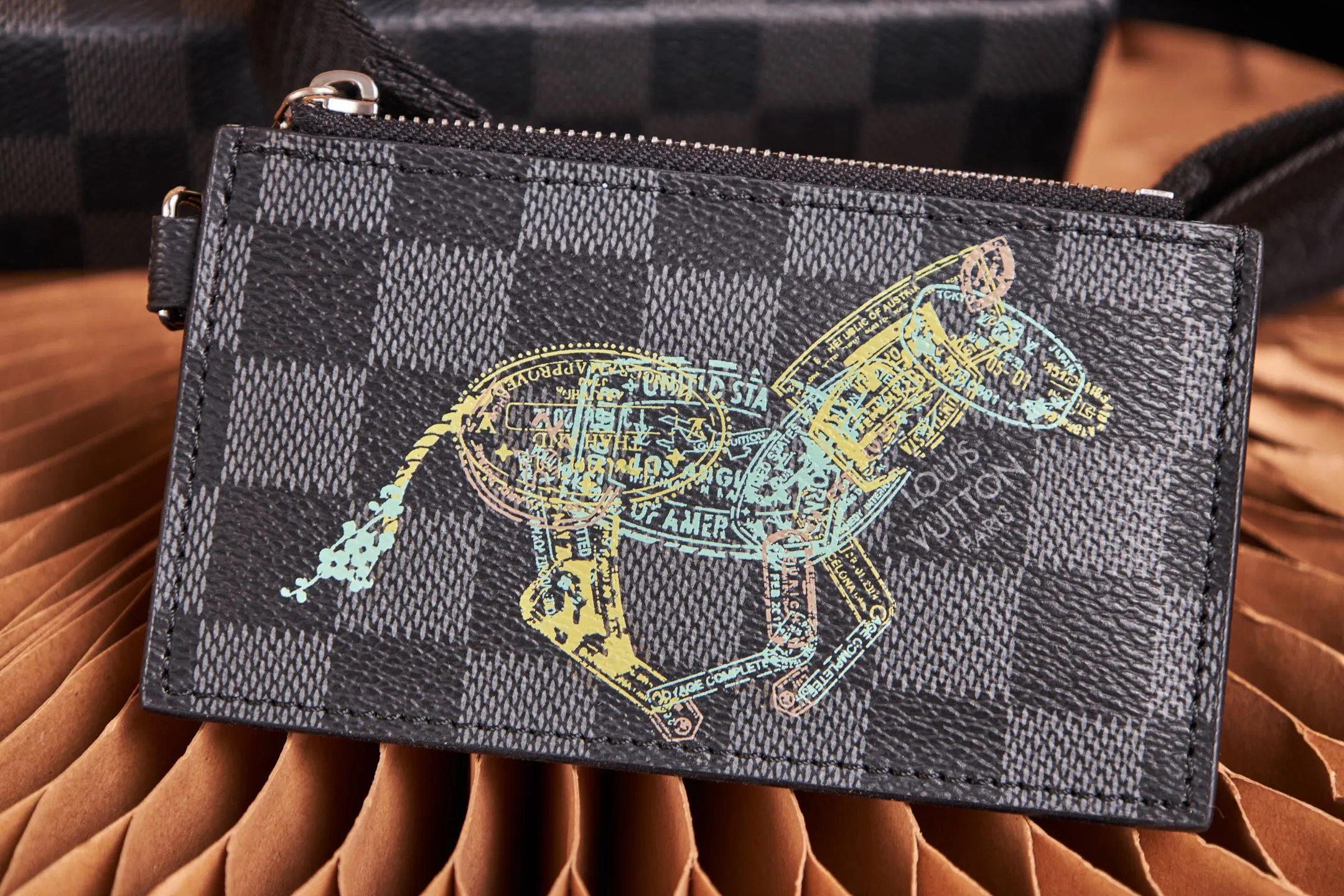 P¥640 [Top Original Order] N64608 This cross-body clutch and dual-use Gaston Wearable Wallet handbag is made of Damier Graphite canvas, with a customs seal-style pattern on the checkerboard surface to show the scene of charging elephants, tigers and ostriches. A removable card holder attached to the shoulder strap allows for touch-free payment. Dimensions: 22 x 14.5 x 4.5 cm