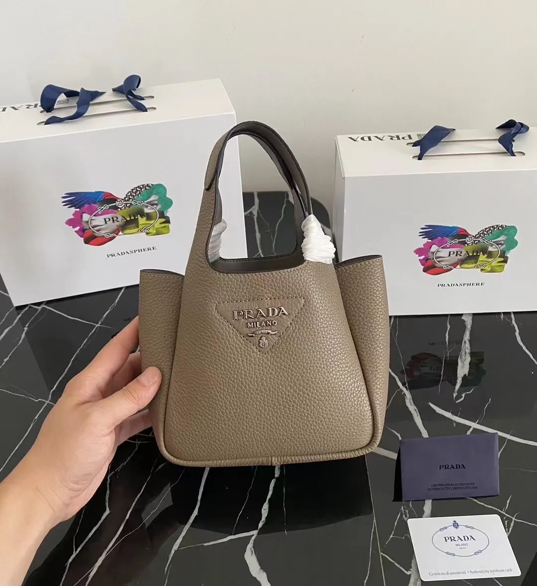 P1100¥ [Top original order] The latest 2022 vegetable basket tote bag mini model 1BA349 has arrived🎉🎉Soft and delicate pebbled calfskin tote bag, full leather inside and outside, equipped with double handles, decorated with silver metal logo, the overall body of the bag is very soft Lightweight, elegant and outstanding. The two side pockets not only meet the needs of exquisite storage but also add an elegant charm. It can be carried as a handbag or an armpit bag. It is a must-have handbag for fairies that perfectly combines classic heritage with the trend of the times. Size: 18︸15.5︸10CM!