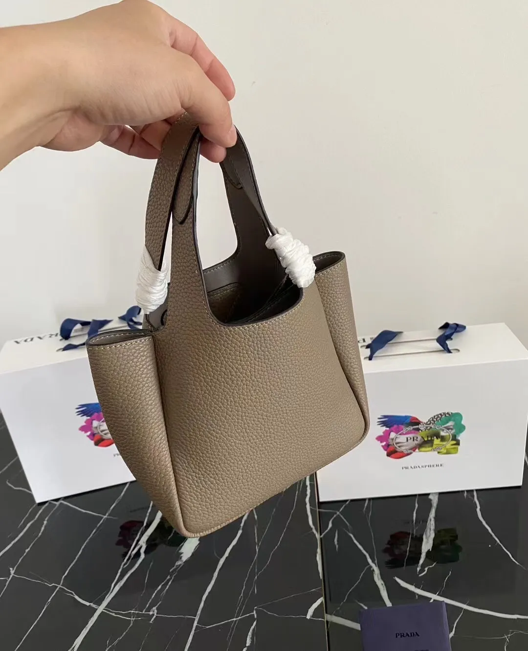 P1100¥ [Top original order] The latest 2022 vegetable basket tote bag mini model 1BA349 has arrived🎉🎉Soft and delicate pebbled calfskin tote bag, full leather inside and outside, equipped with double handles, decorated with silver metal logo, the overall body of the bag is very soft Lightweight, elegant and outstanding. The two side pockets not only meet the needs of exquisite storage but also add an elegant charm. It can be carried as a handbag or an armpit bag. It is a must-have handbag for fairies that perfectly combines classic heritage with the trend of the times. Size: 18︸15.5︸10CM!
